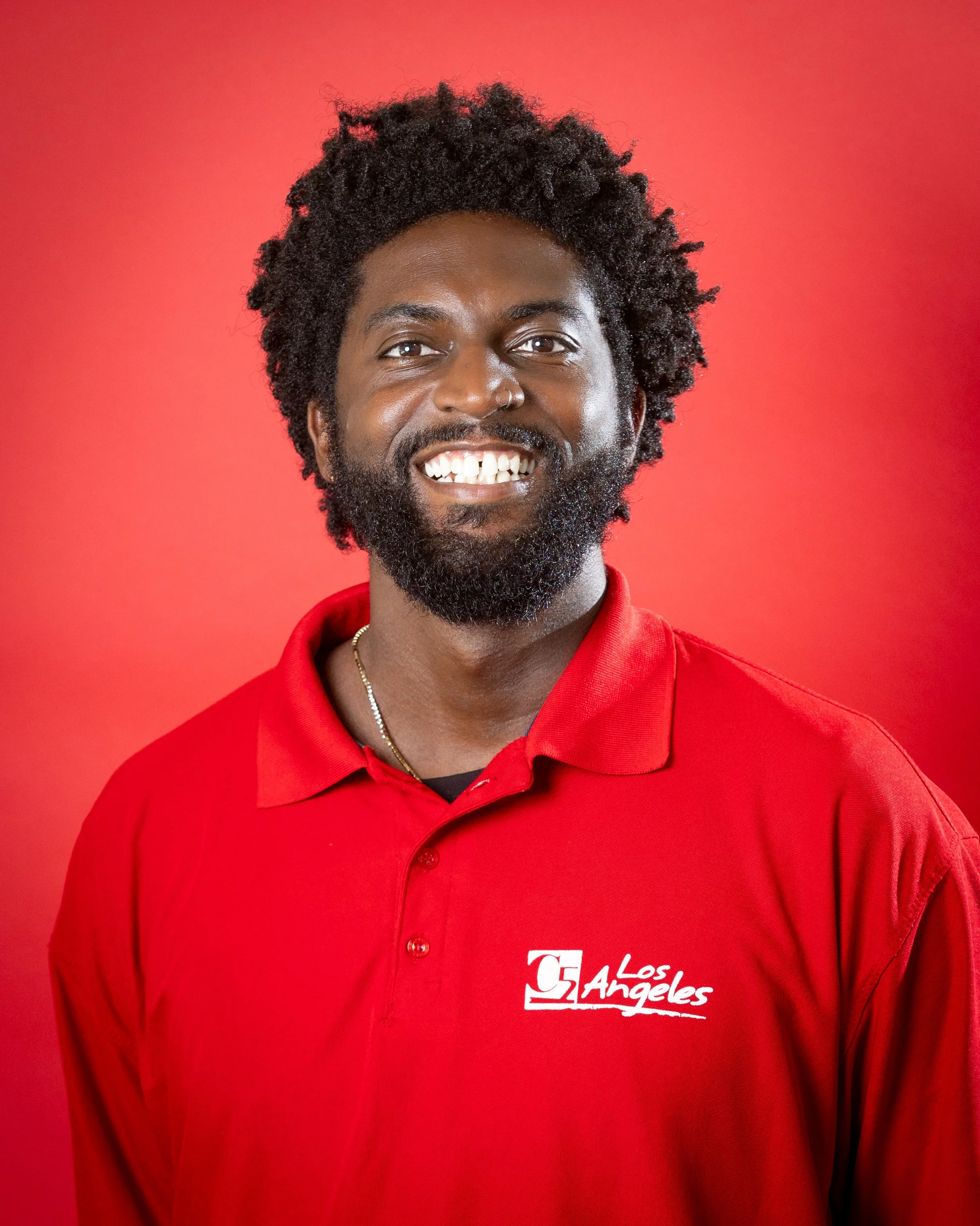 Smiling man with curly hair and a beard, wearing a red polo shirt with the C5 Los Angeles logo.