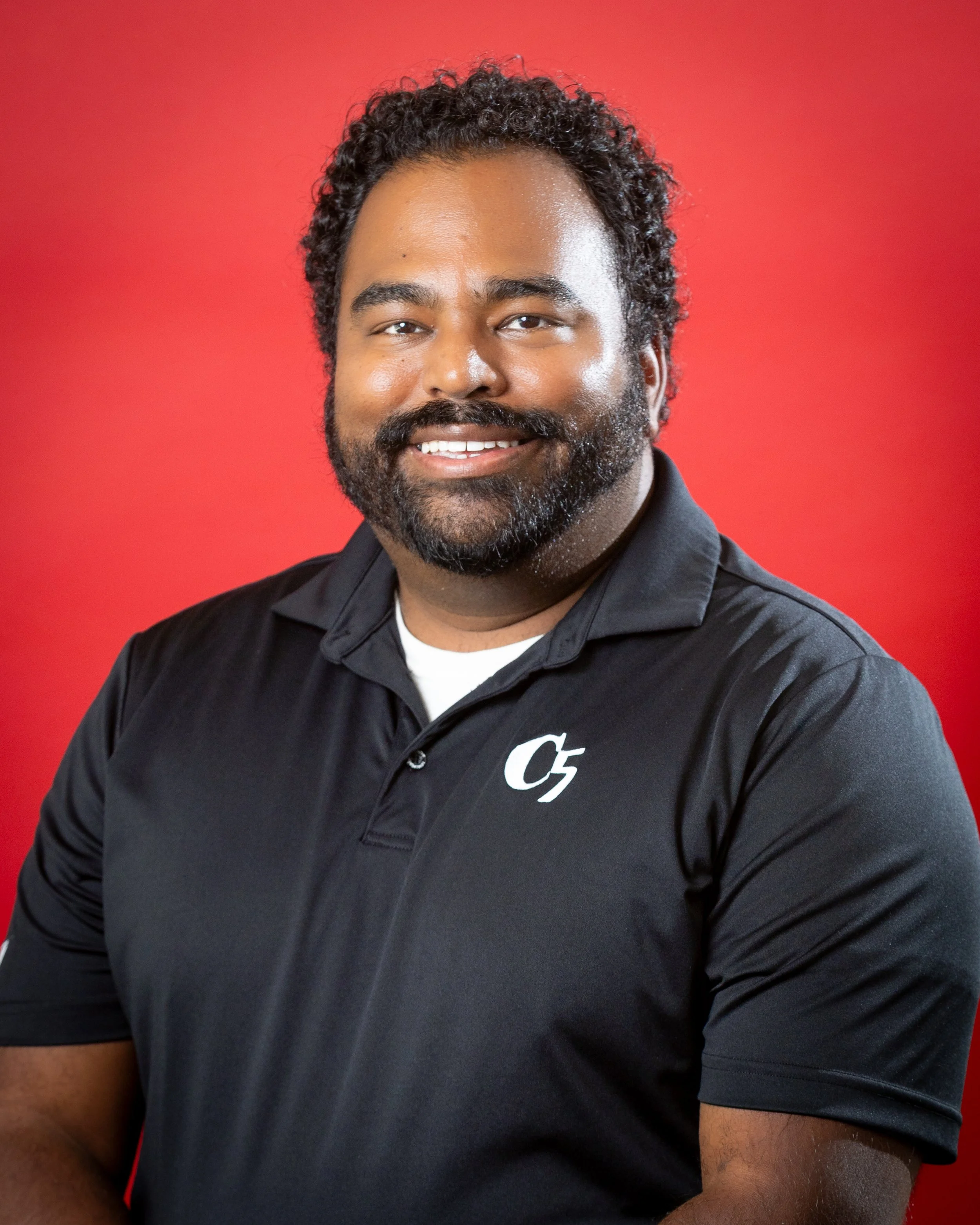 A man with curly hair wearing a black polo with the C5 logo.