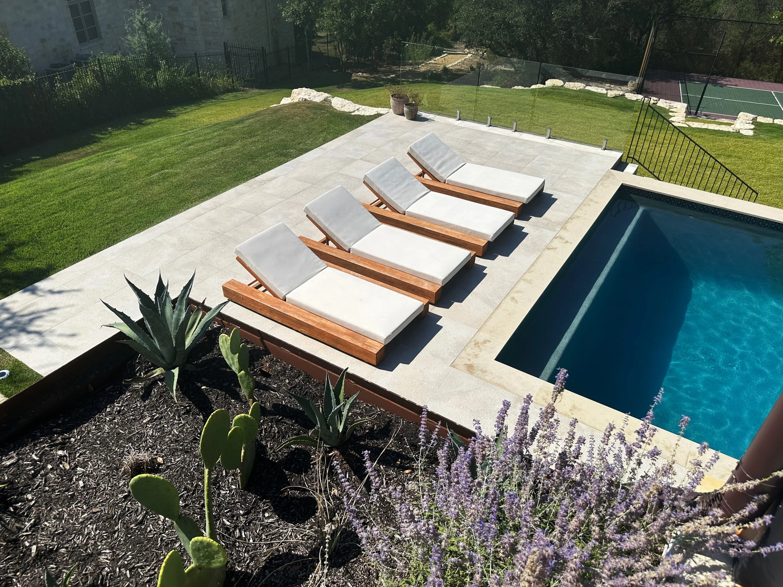 Aerial view of four wood chaise loungers beside a modern pool with agave and lavender in a corten steel planter
