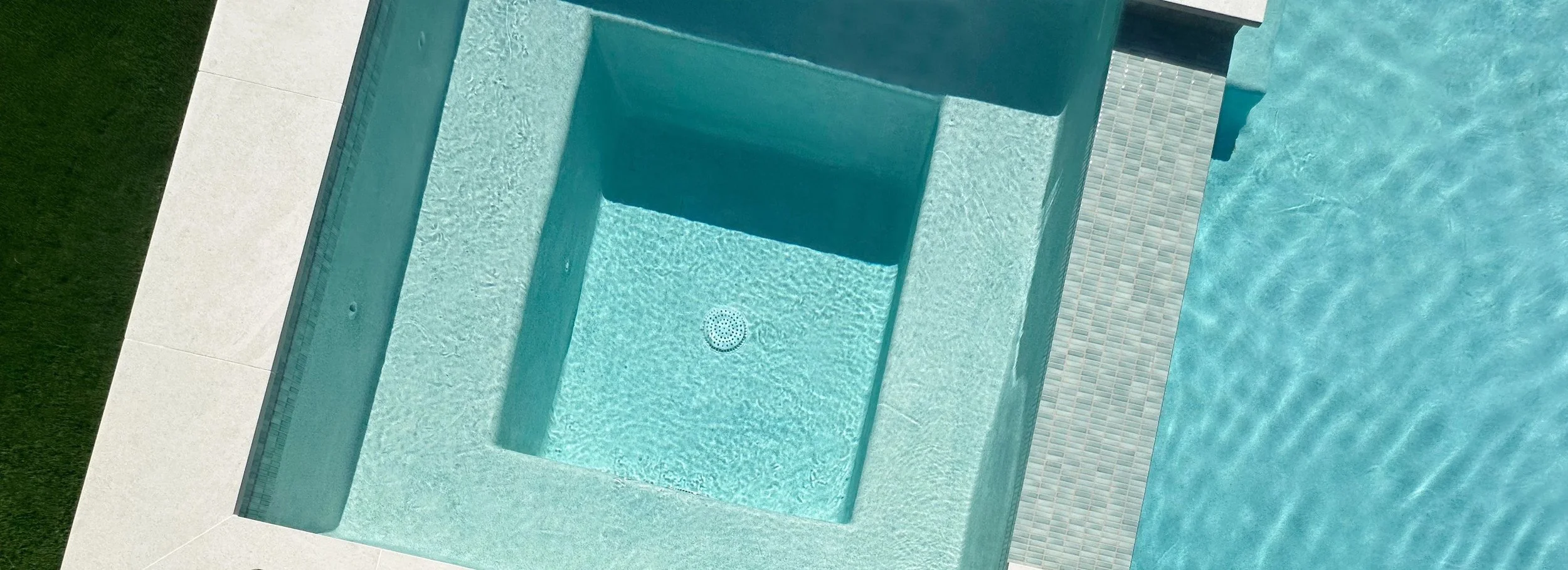 Looking down into a raised spa with glass tile band, interior bench, and Cayman Green pebble floor