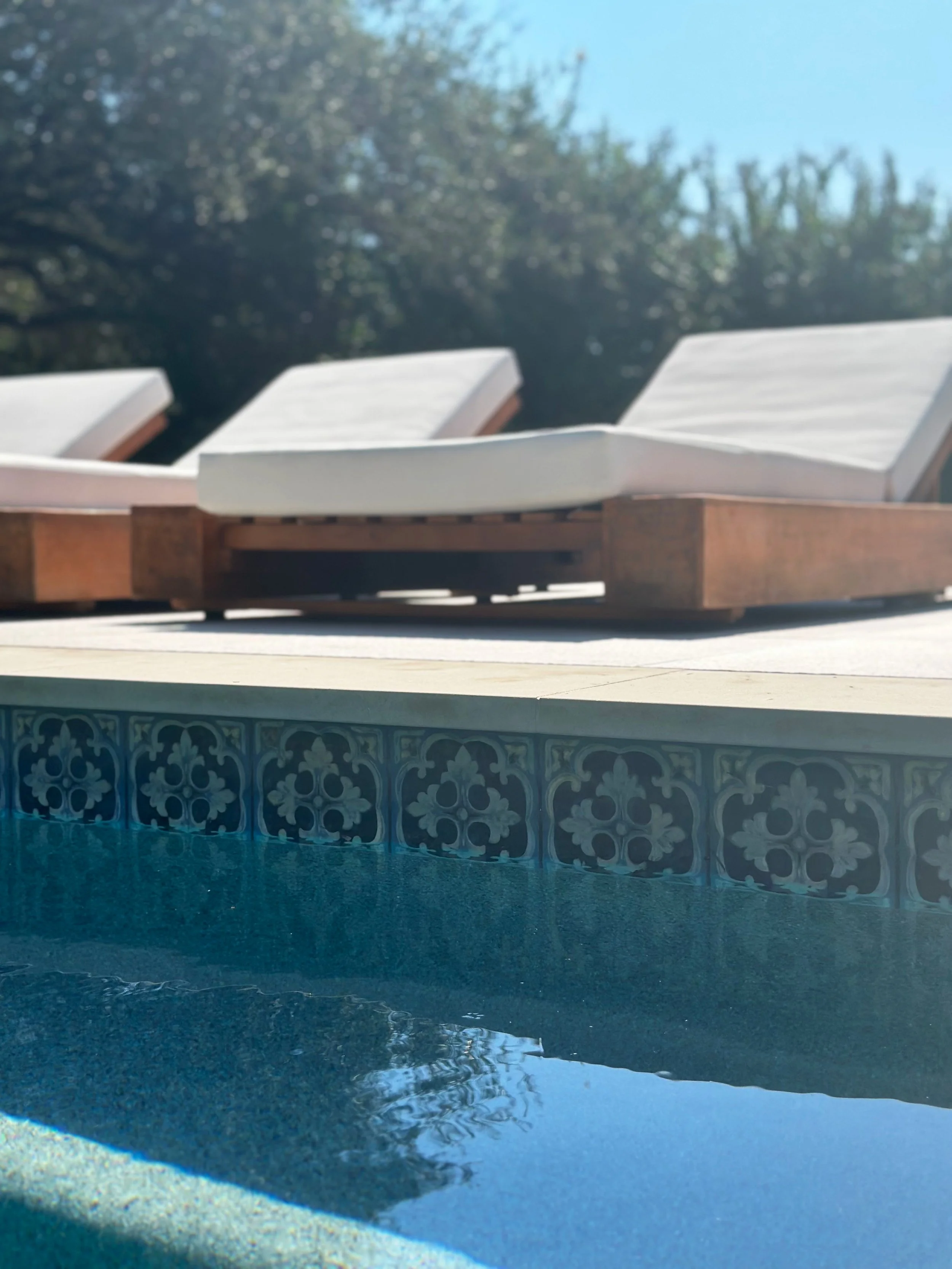 Waterline detail of blue and white NPT Hana Capri tile with wood chaise loungers poolside