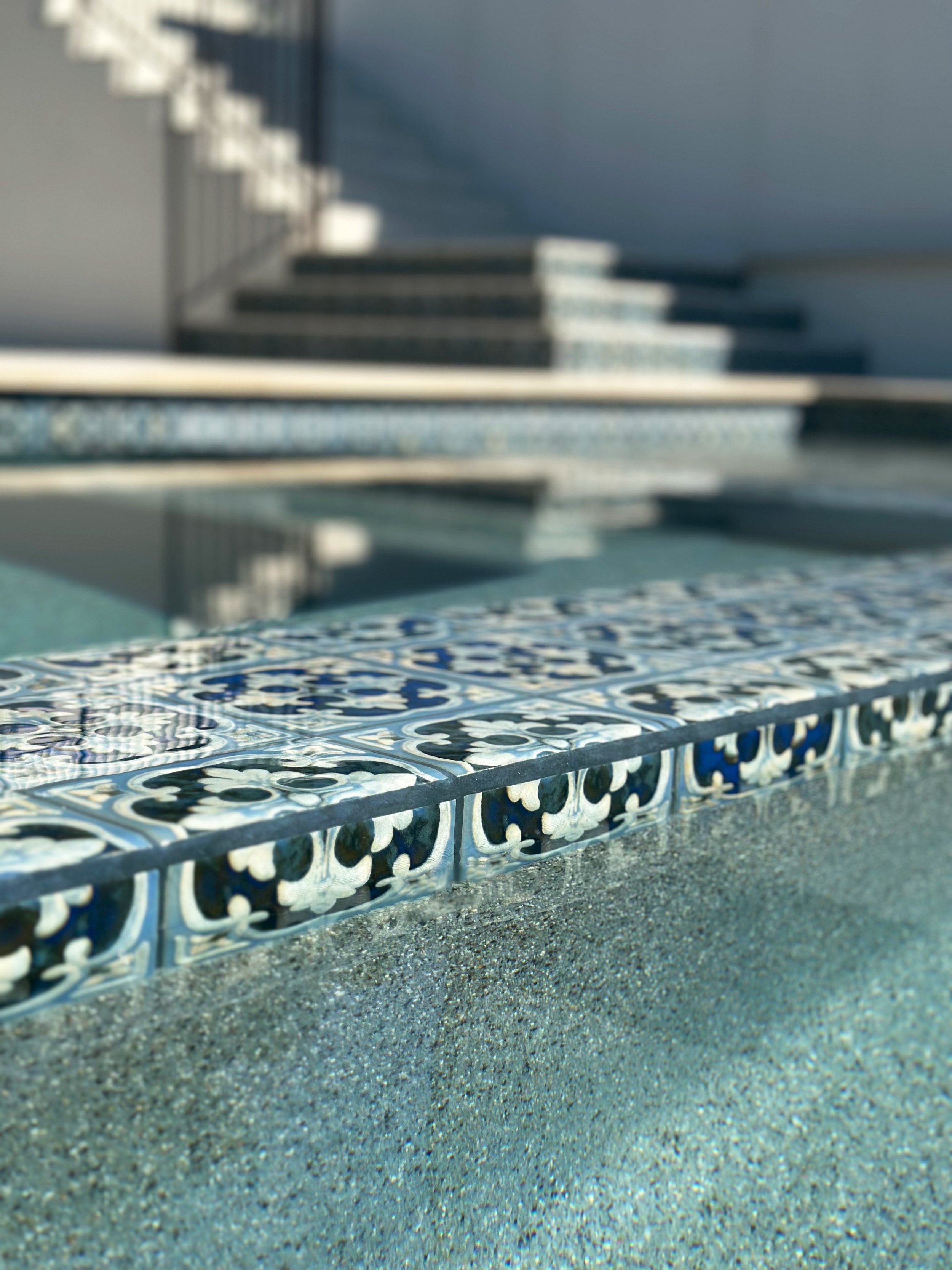 Detail shot of tiled pool steps and sun shelf with blue and white Spanish tile and pebble finish