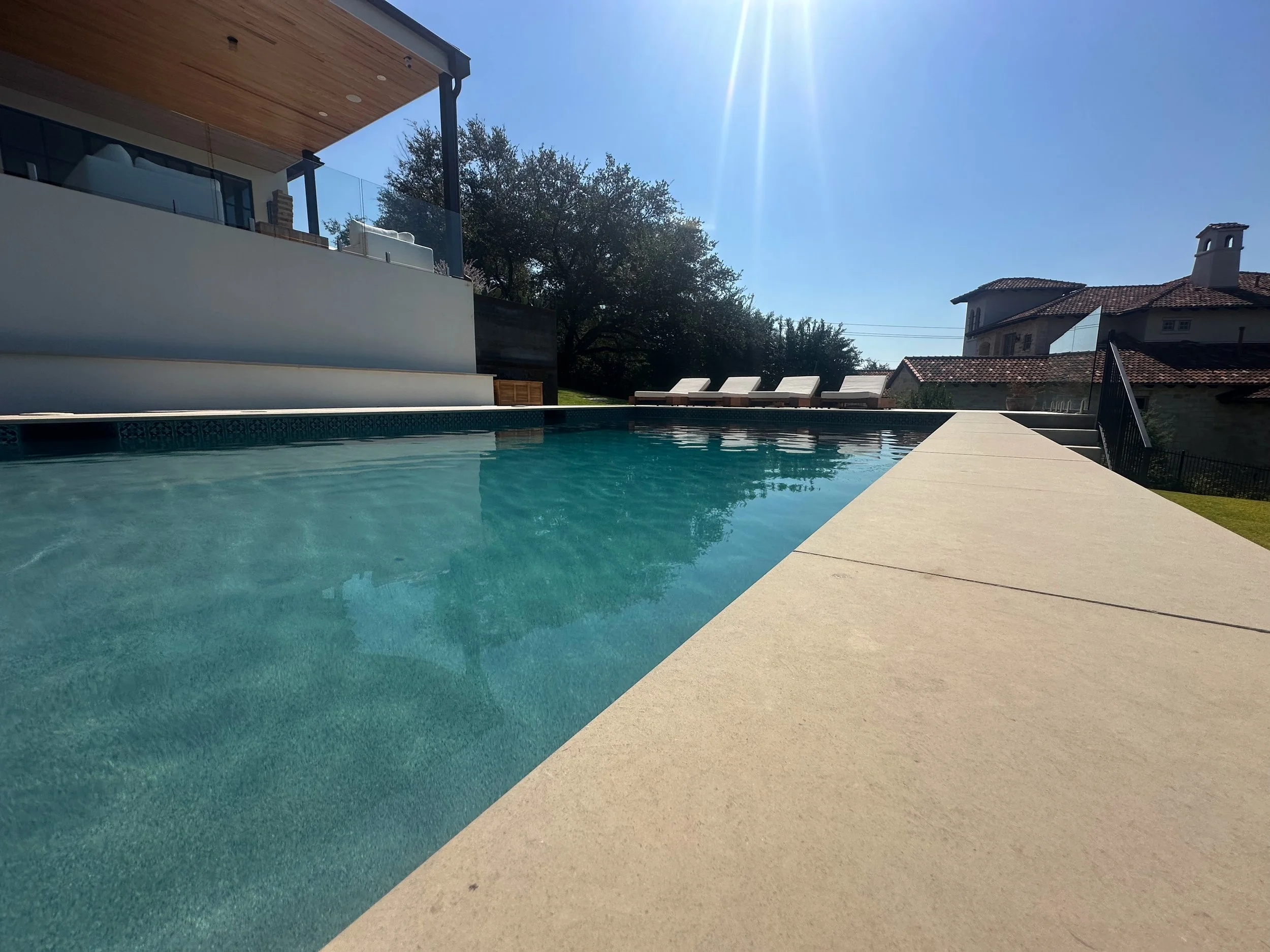 Modern luxe pool with buff Lueders stone deck beside a contemporary Austin Hill Country home