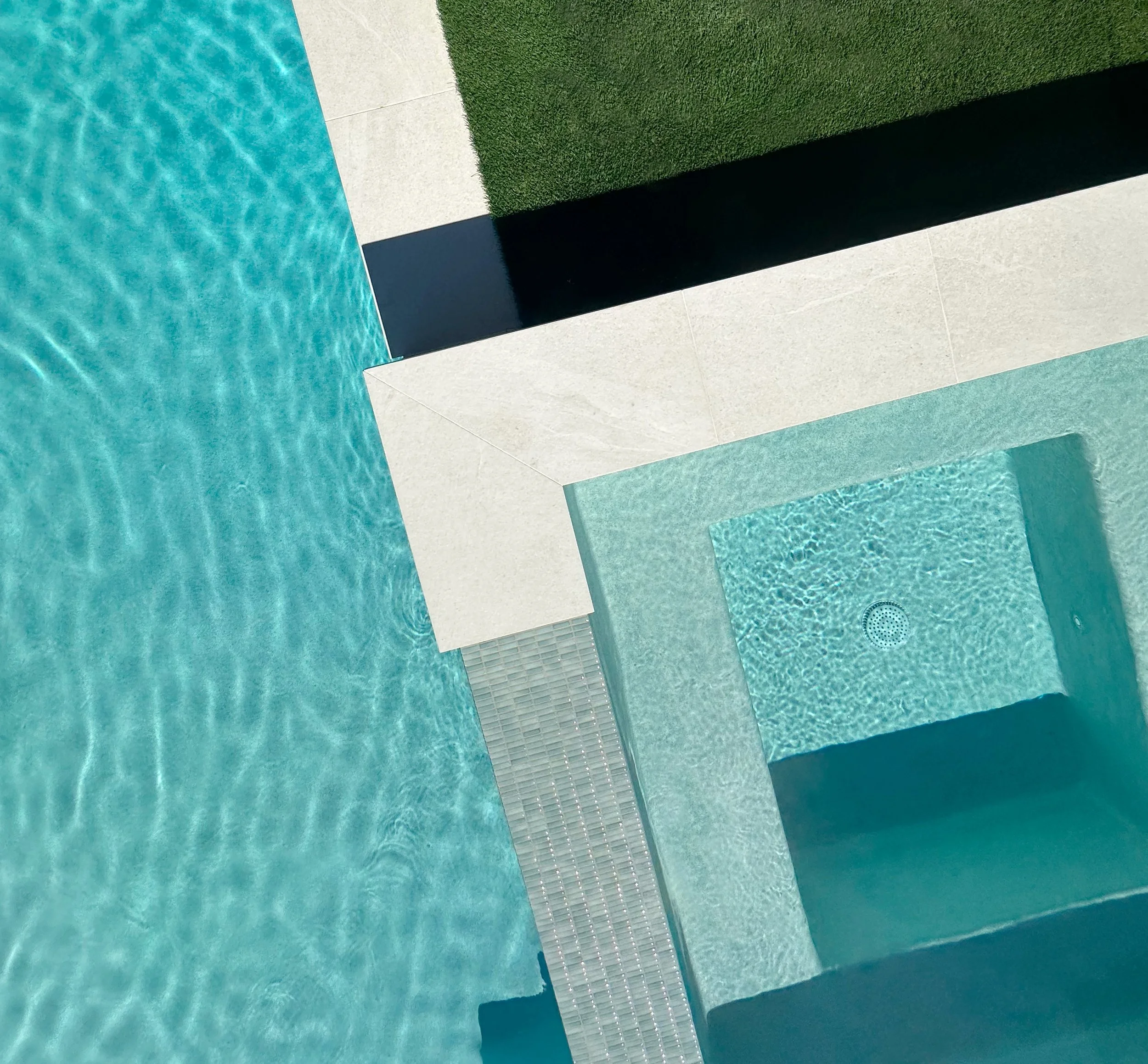 Close overhead of a raised spa's tiled spillover edge and submerged bench with Cayman Green interior finish
