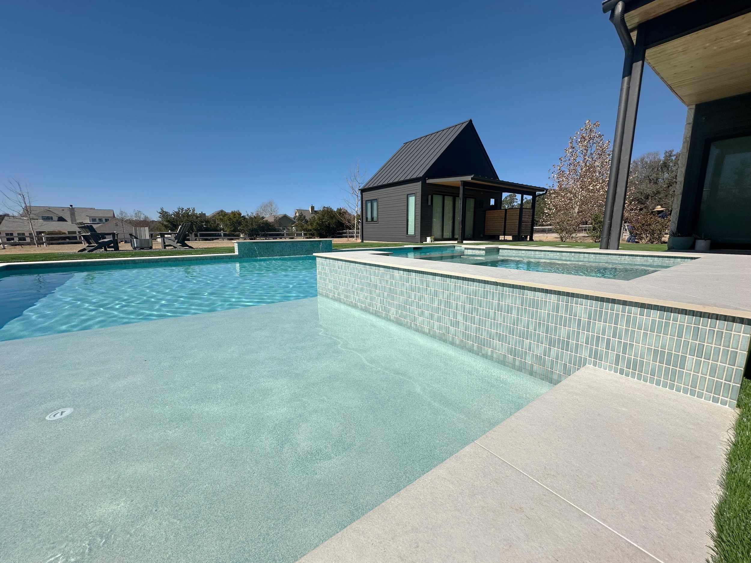 Low view of a raised spa wall in Cepac Krave Straight Set Basil green glass tile with sun shelf and casita behind