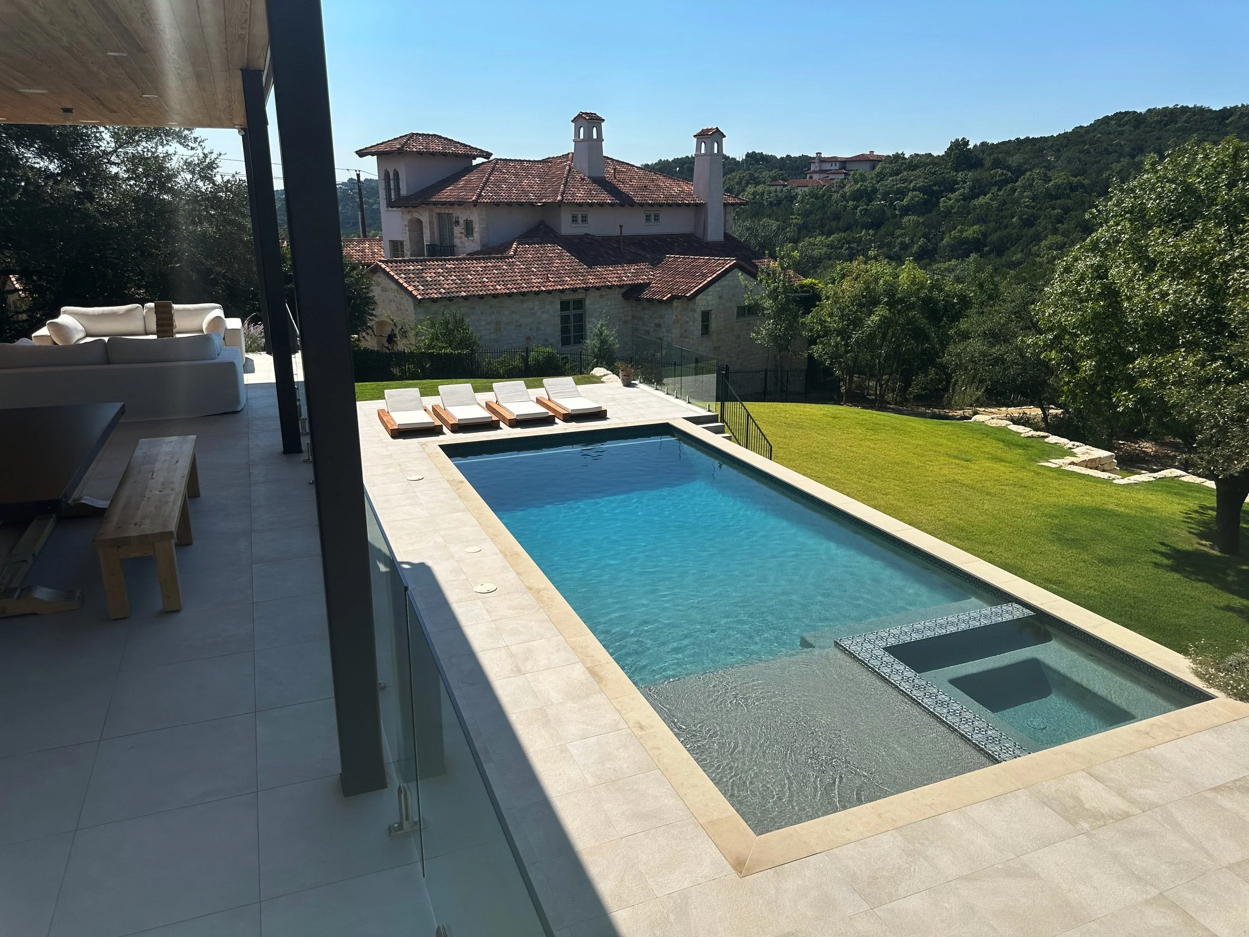 Modern luxe pool and spa viewed from a covered patio with Hill Country hills beyond