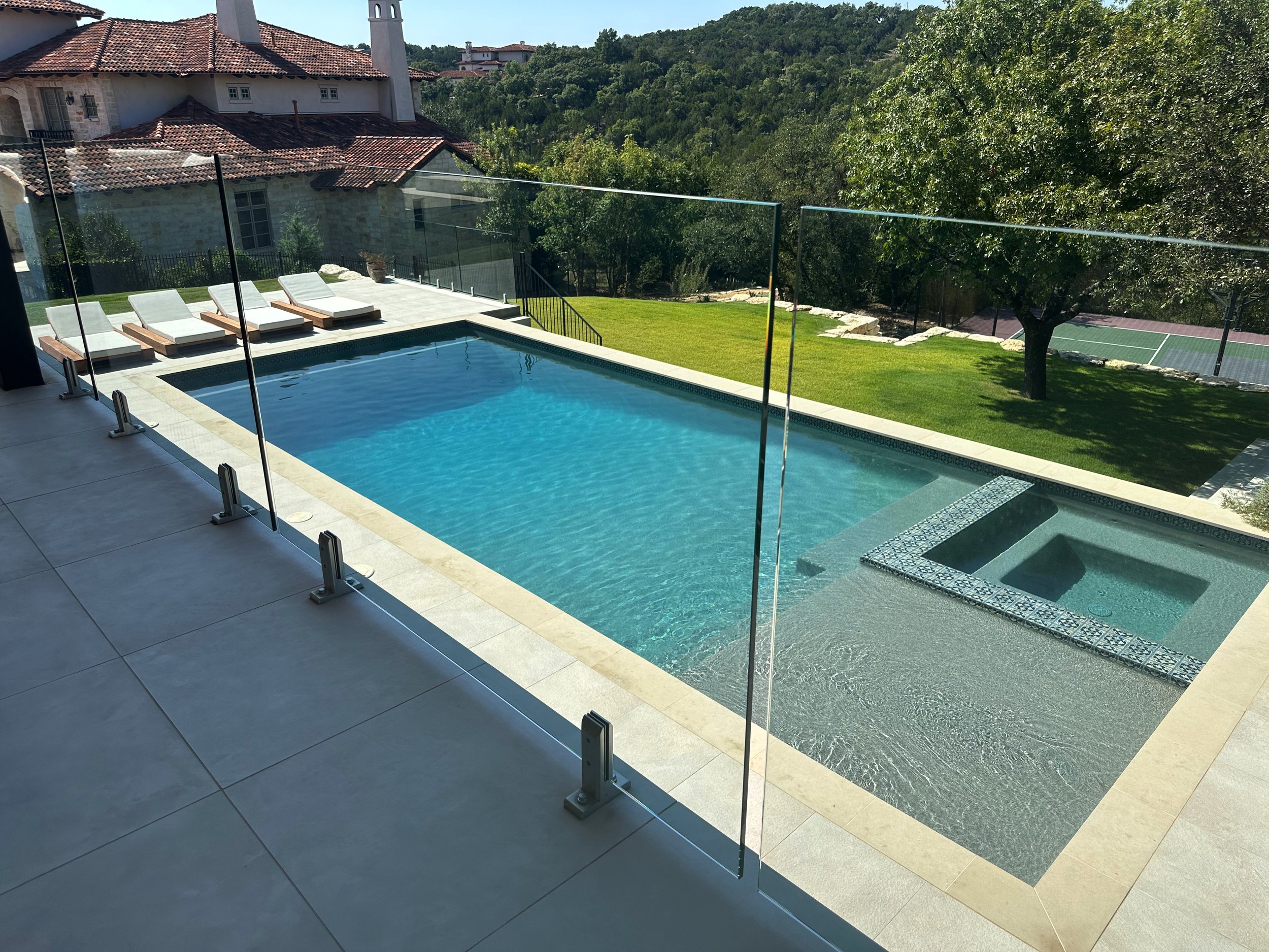 Modern luxe pool and tiled spa behind a frameless glass railing with Hill Country views
