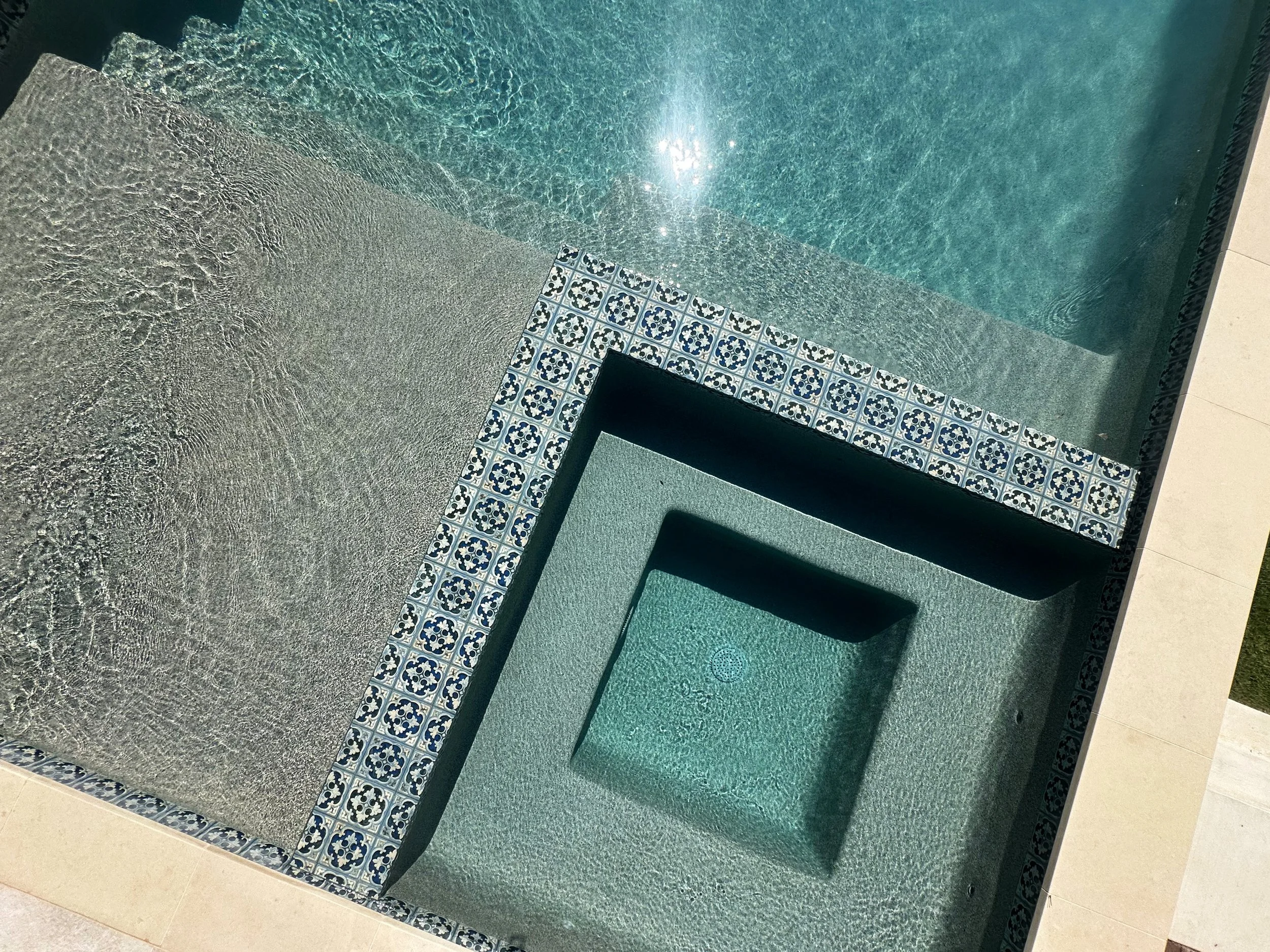 Overhead detail of a flush spa with blue and white Hana Capri tile and French Gray pebble finish