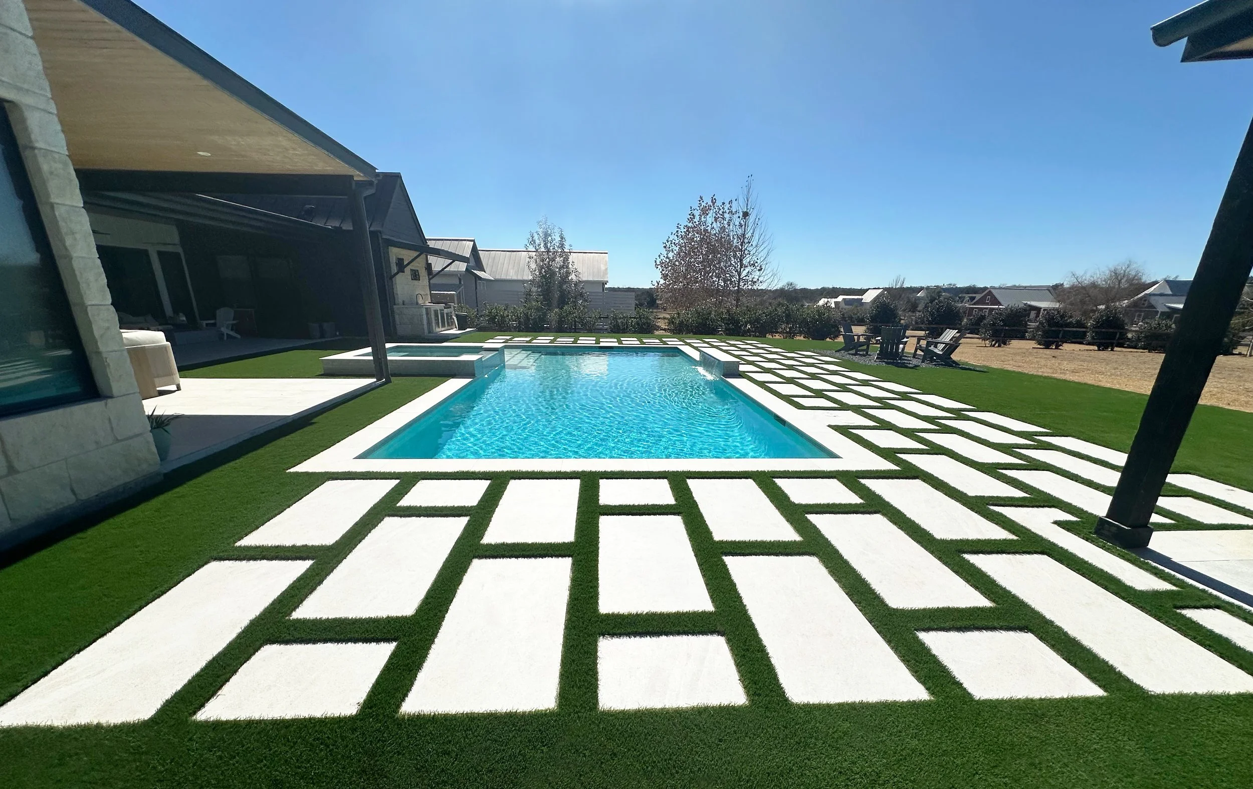 Modern farmhouse pool framed by a Del Conca USA New England White paver-and-turf grid with covered patio and lawn