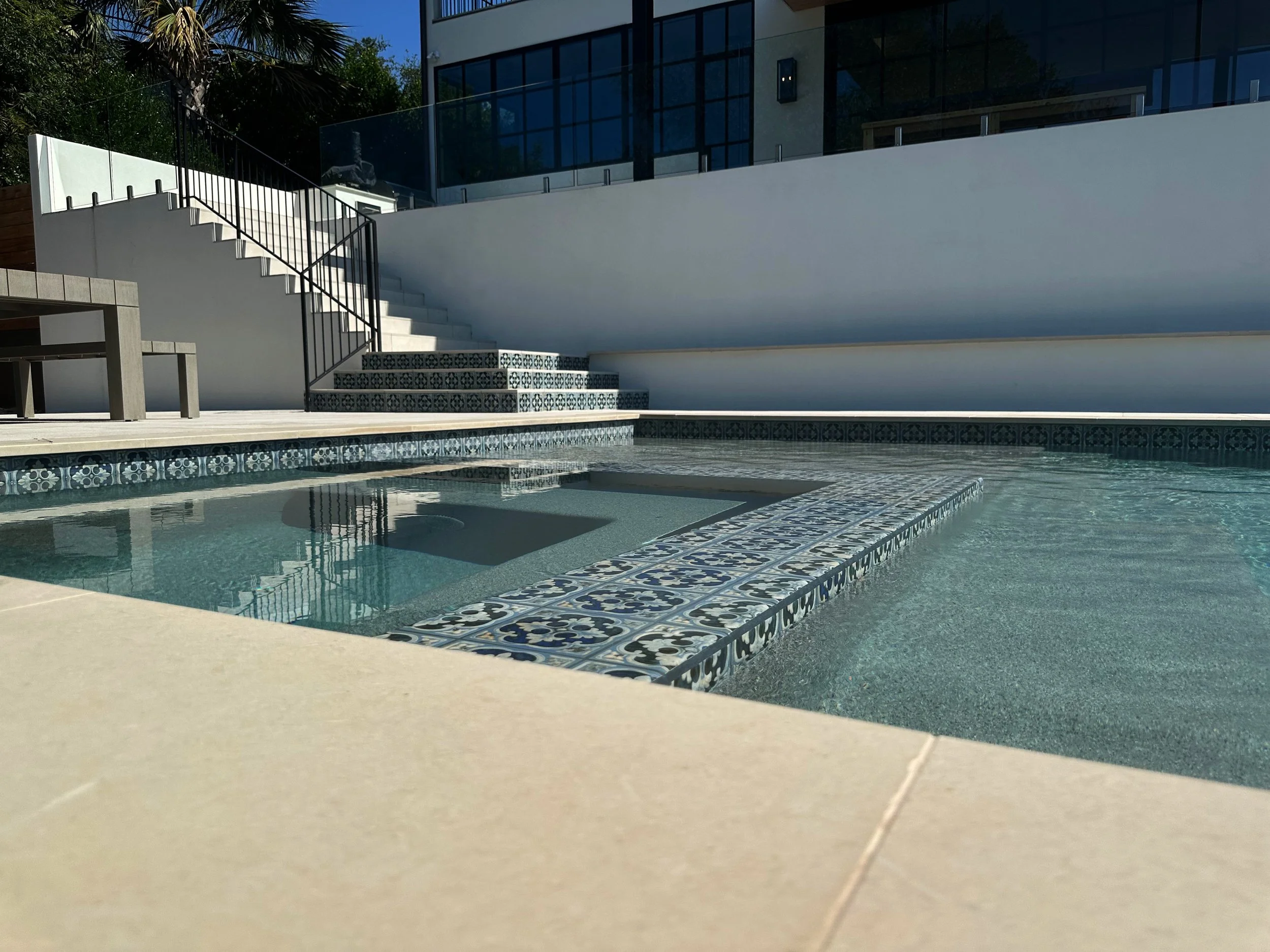 Built-in bench seating with patterned Spanish tile and French Gray pebble inside a modern pool