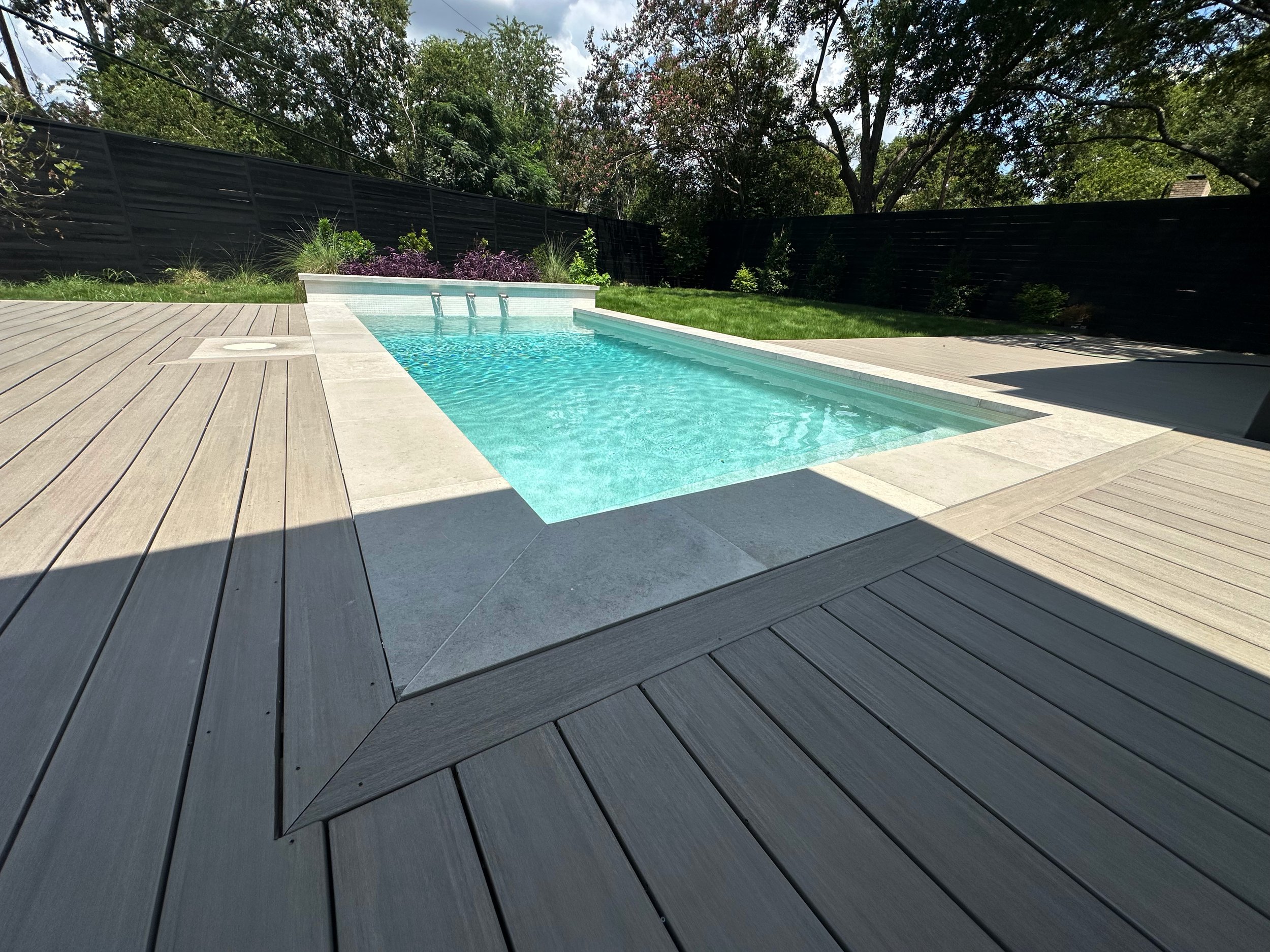 Modern pool with raised water feature wall framed by a two-tone geometric composite deck