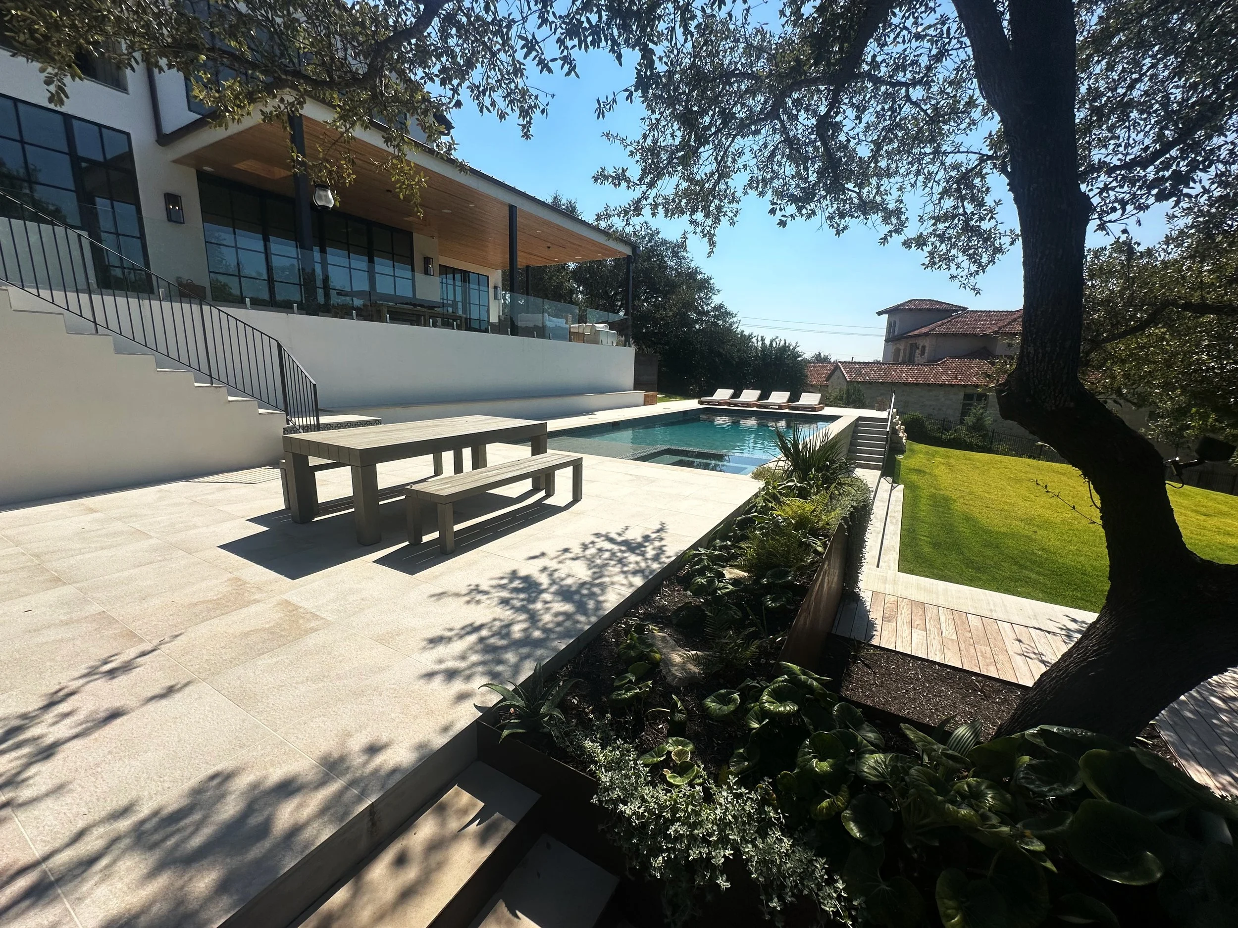 Modern luxe pool and stone patio with corten steel planters shaded by a live oak in the Texas Hill Country