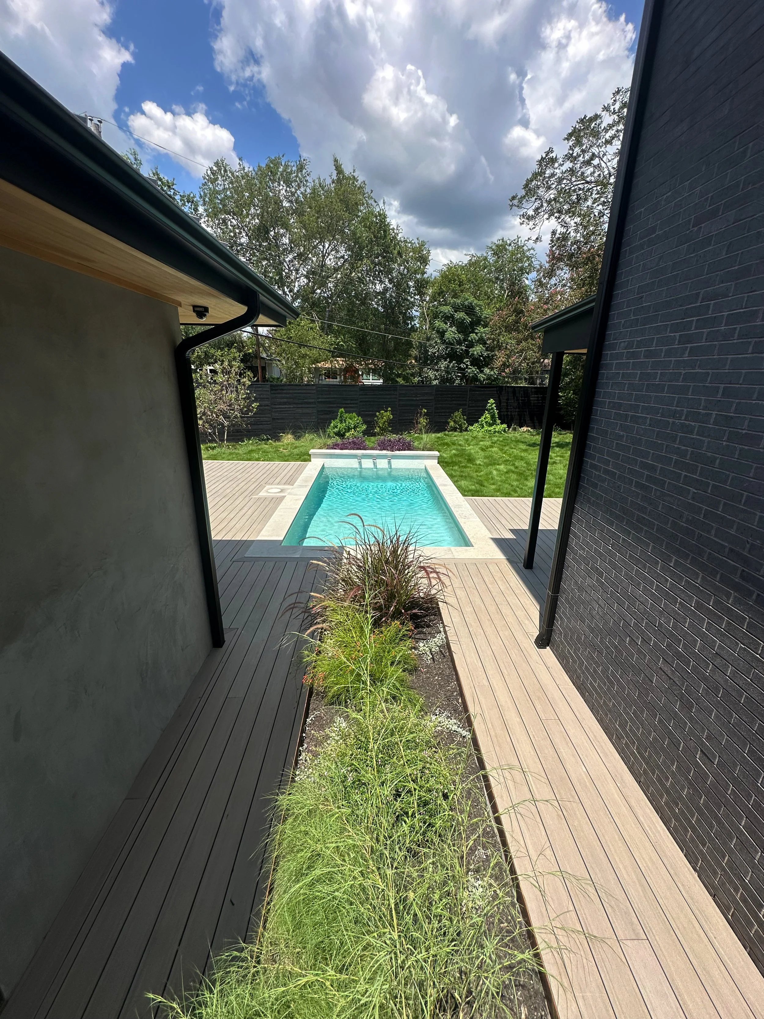 Modern pool and raised water feature wall viewed through a breezeway between stucco and brick walls