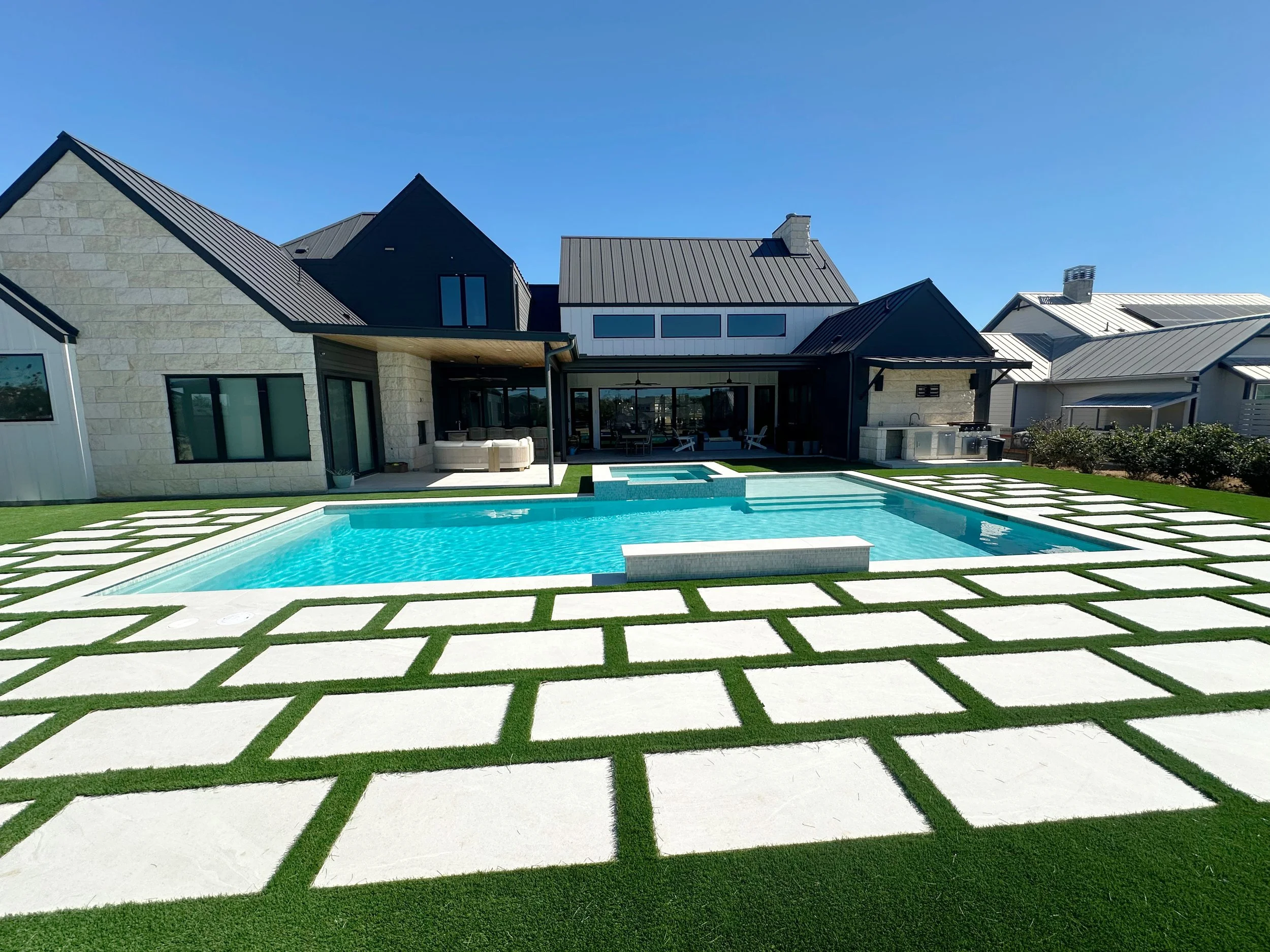 Rear elevation of a modern farmhouse home with a rectangular pool, raised spa, and outdoor kitchen