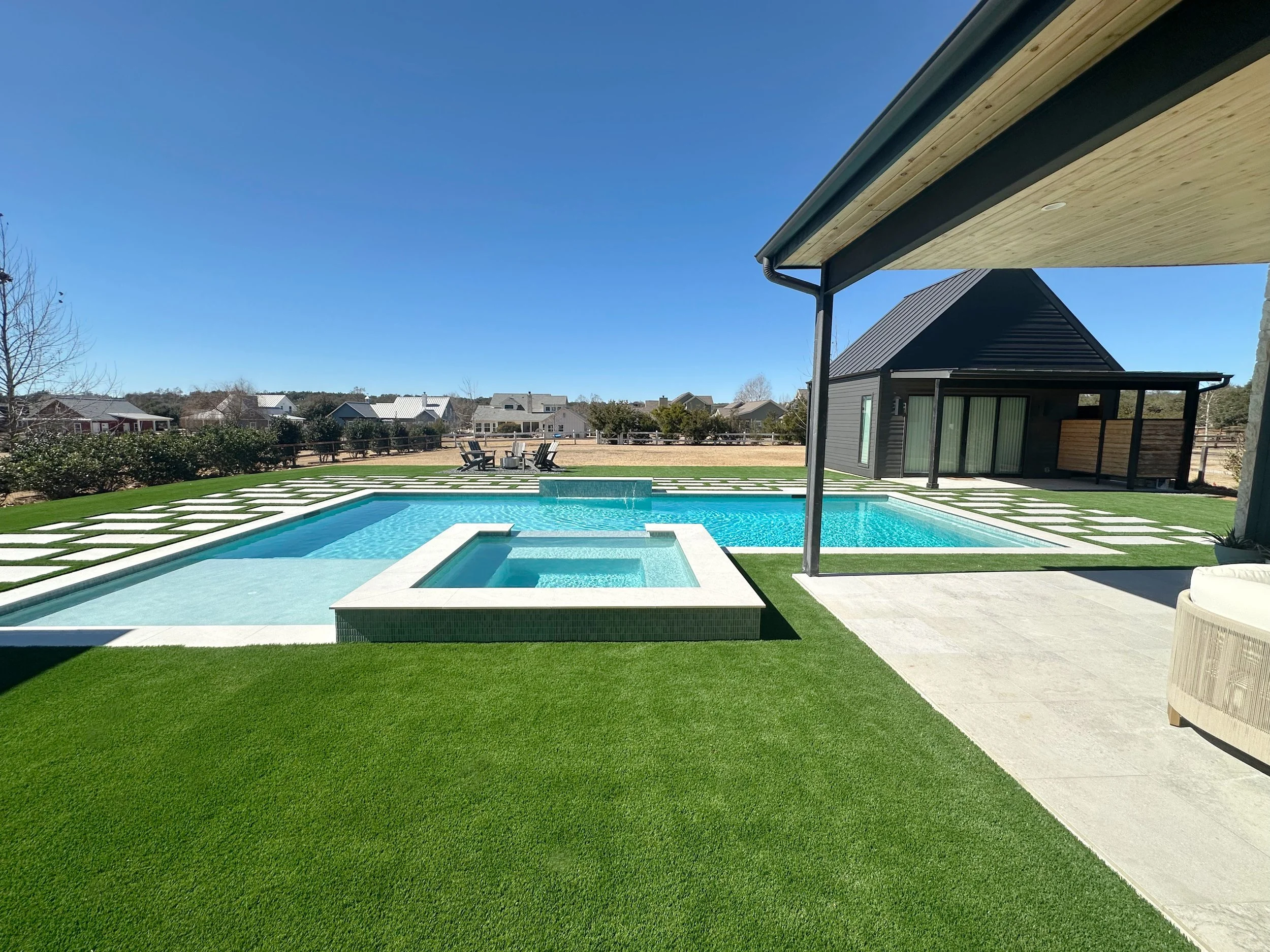 Modern farmhouse pool and raised spa framed by open turf lawn with casita and covered patio