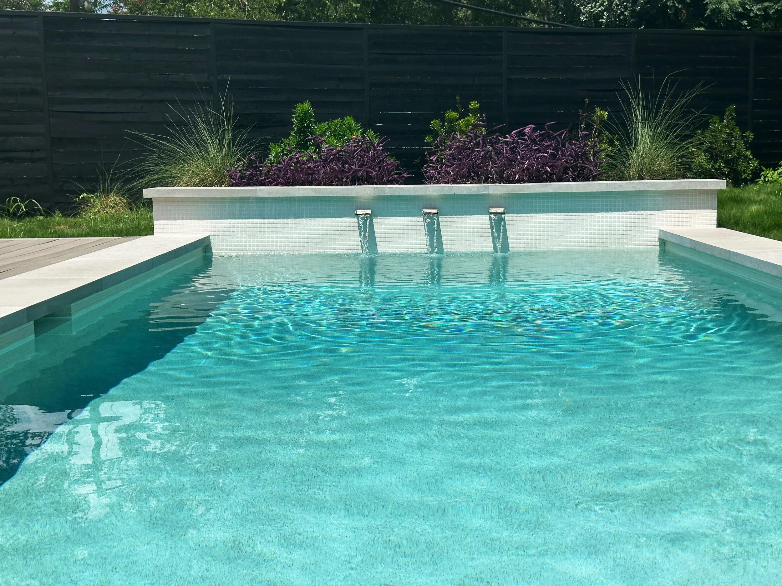 Modern pool with triple scuppers and a raised planter wall of purple heart plants
