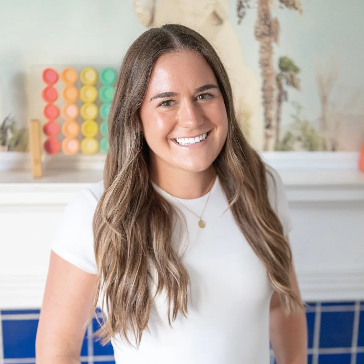 Madison Wall with long brown hair and a white shirt smiling indoors with a colorful bubble tea setup in the background.