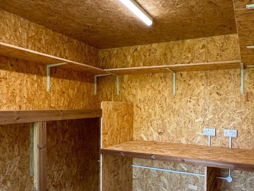 Interior of an integrated garden room storage area with plywood walls, electrical sockets and lighting.