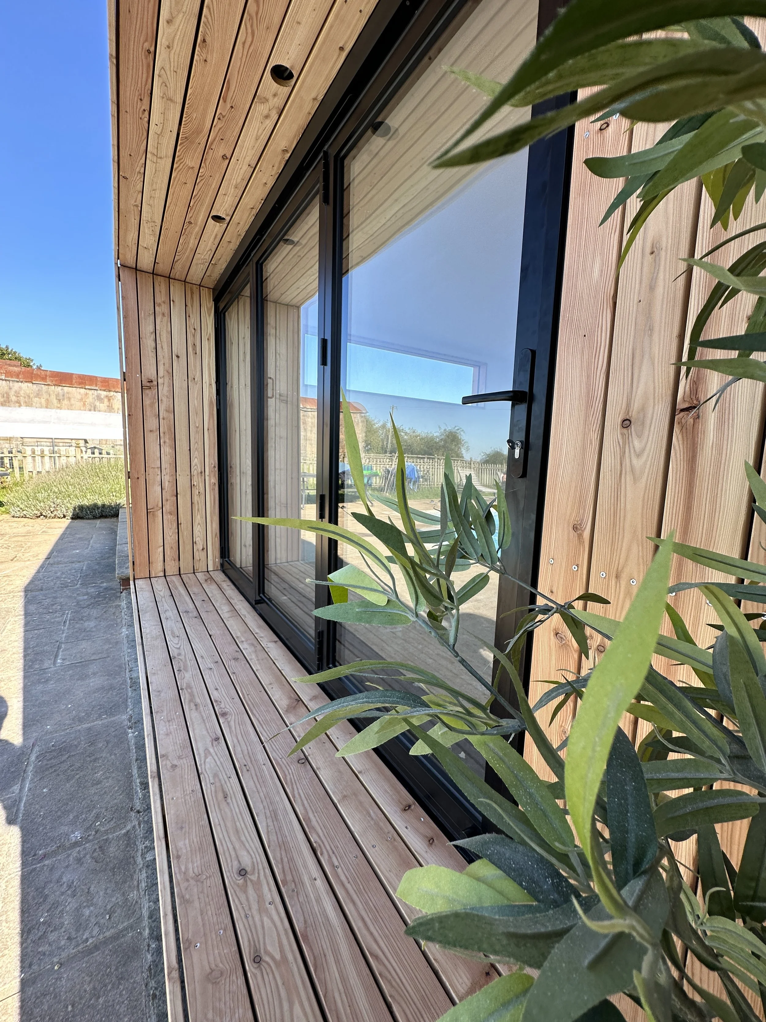 Angled exterior view of the FORZA garden room showing the front porch, double-glazed doors, external cladding, and surrounding garden
