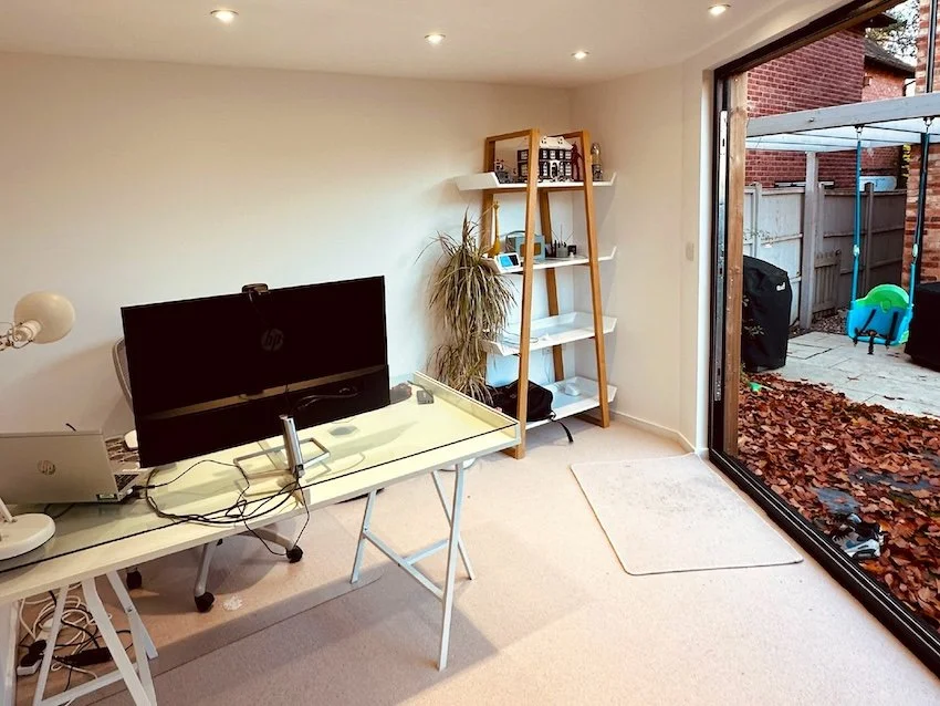 Carpeted bespoke garden office interior with a desk, spotlights and bi-fold doors, designed to maximise the available space.