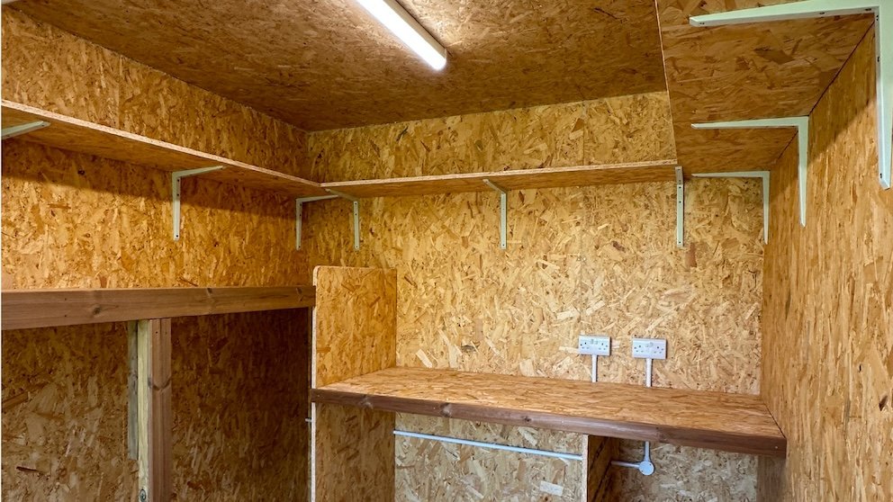 Integrated garden room storage area with a built-in workbench, shelving, lighting and electrical sockets.