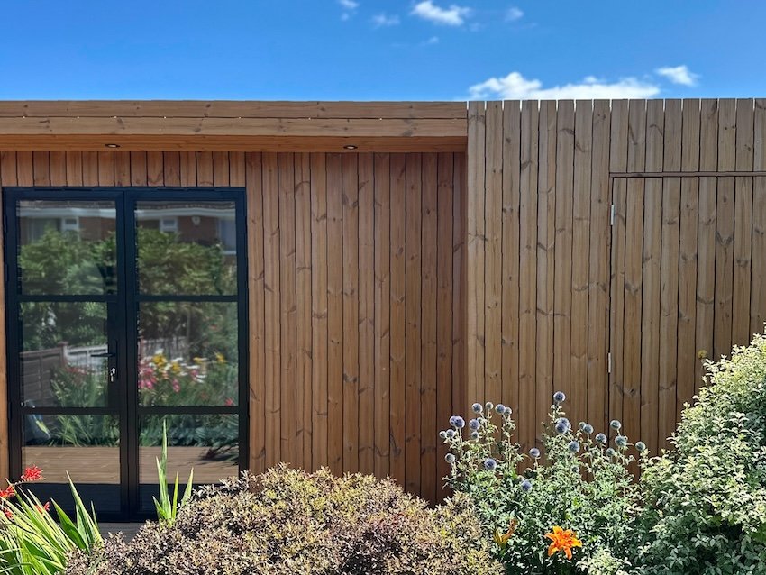 Bespoke garden office and relaxation space with seating and integrated storage concealed behind a matching clad door.