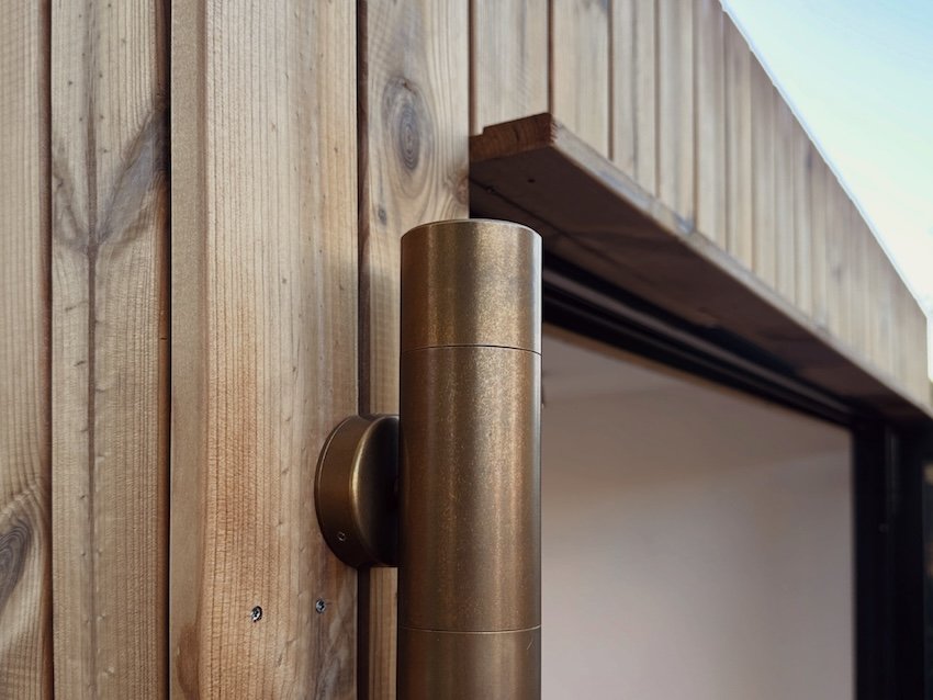 Brass up-and-down exterior wall light fitted beside the garden room’s timber cladding.