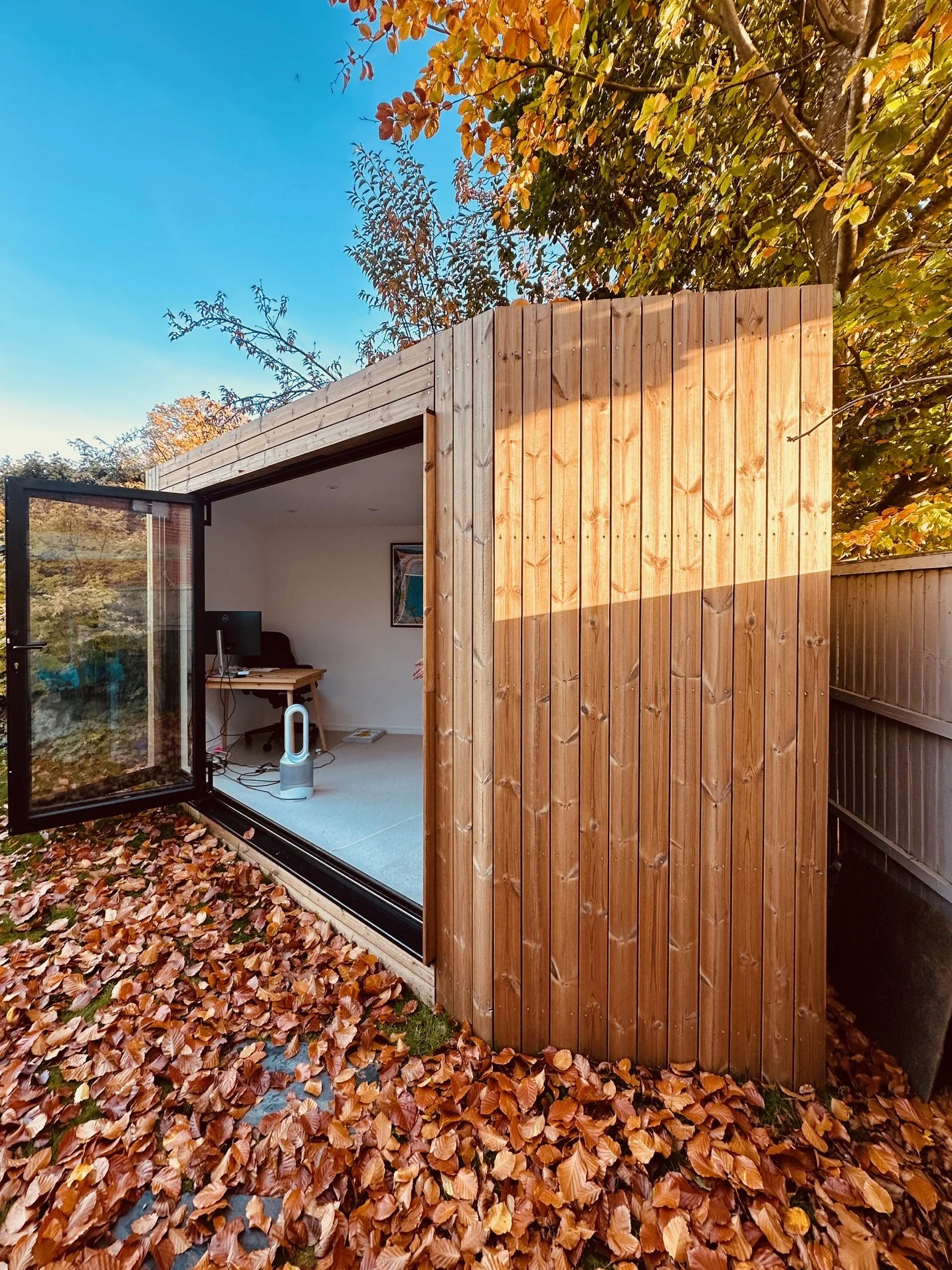 Compact garden office installed in a small garden, with timber cladding and large glazed doors