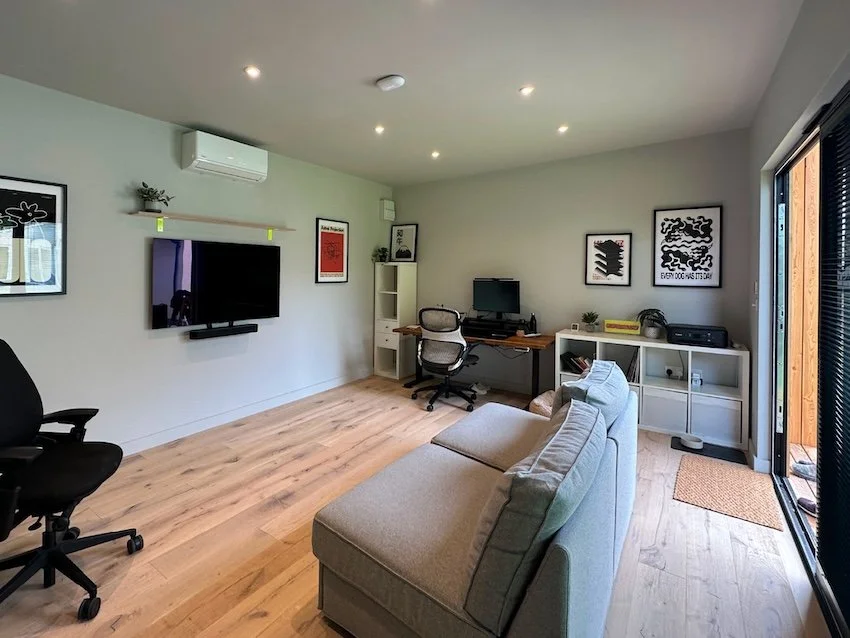 Bespoke multi-use garden room with hardwood flooring, air conditioning, office space, a sofa, television and integral blinds.