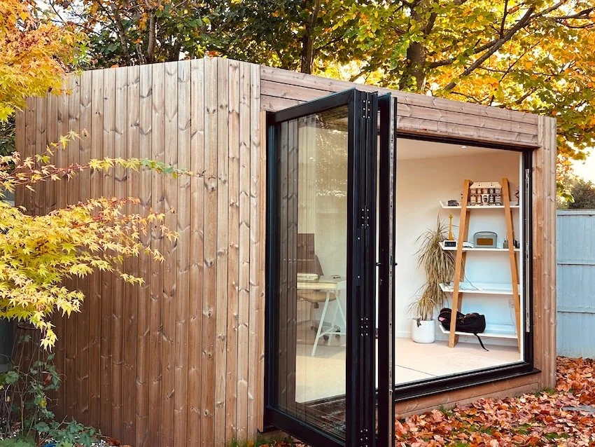 Custom-sized insulated garden office in an autumn garden, designed for comfortable year-round use.