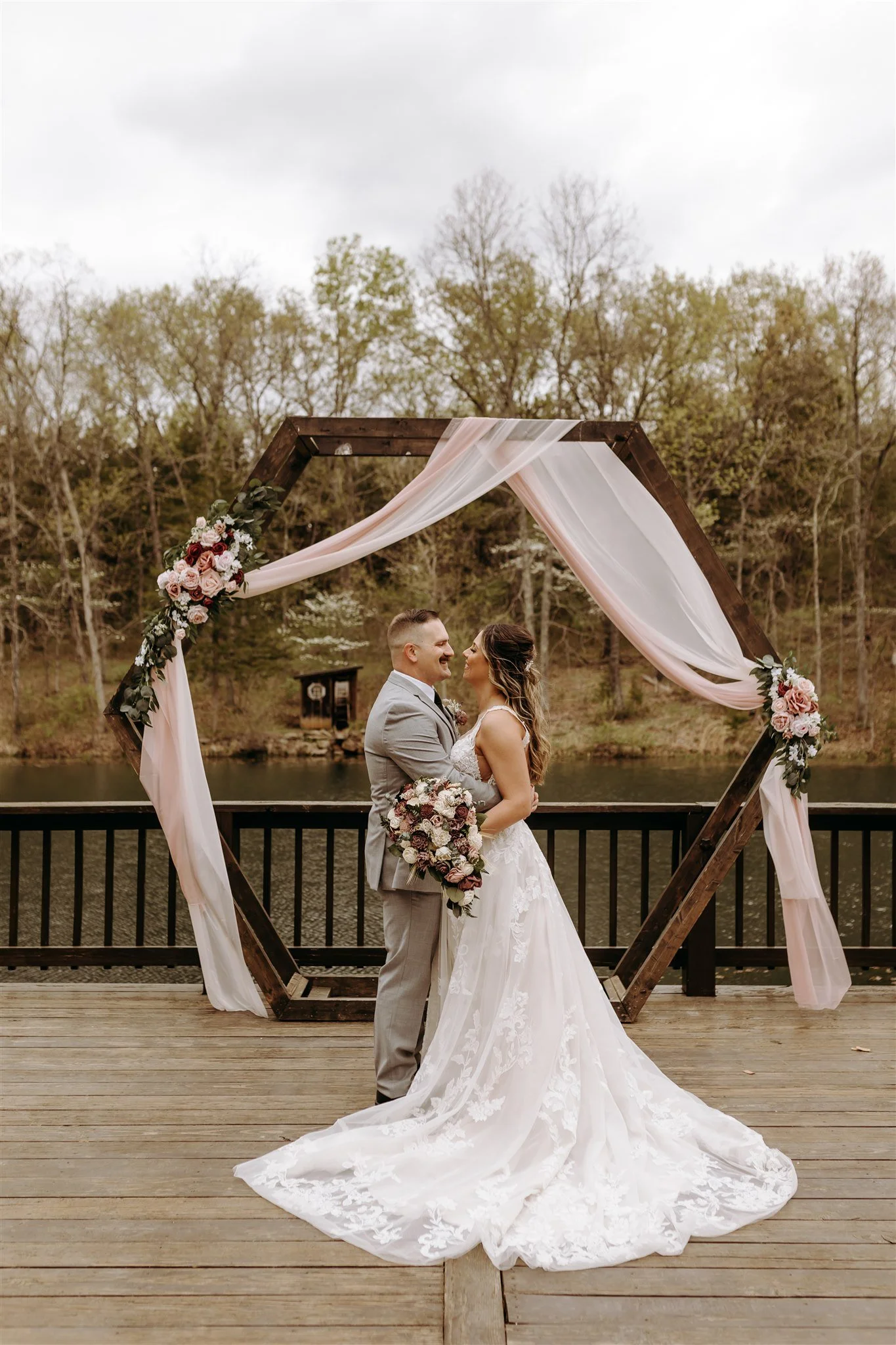 A bride and groom stand on a wooden deck, facing each other and smiling at Rolla, MO rustic wedding venue, The Village. Photos by Columbia, MO Photographer Liv Strange Photography.