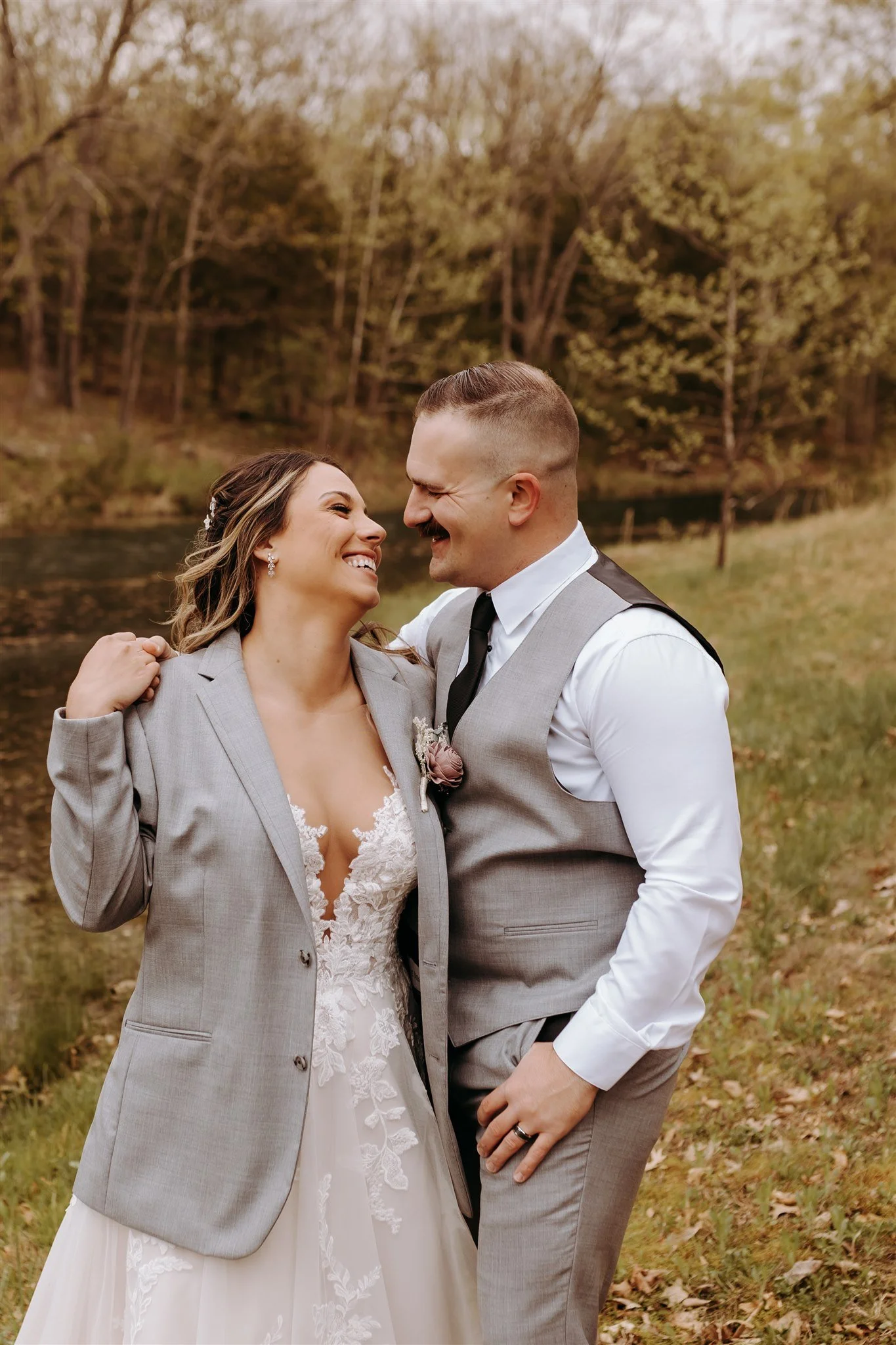 A newlywed couple smiling and embracing outdoors near a river with trees in the background at Rolla, MO rustic wedding venue, The Village. Photos by Columbia, MO Photographer Liv Strange Photography.