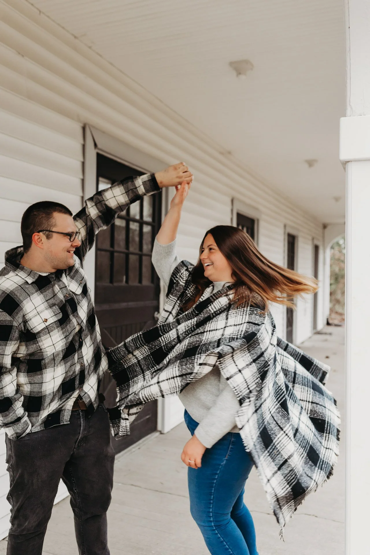 A young couple dancing and enjoying each other's company on a porch, wrapped in matching plaid blankets at their engagement photography session at Queeny Park in STL.