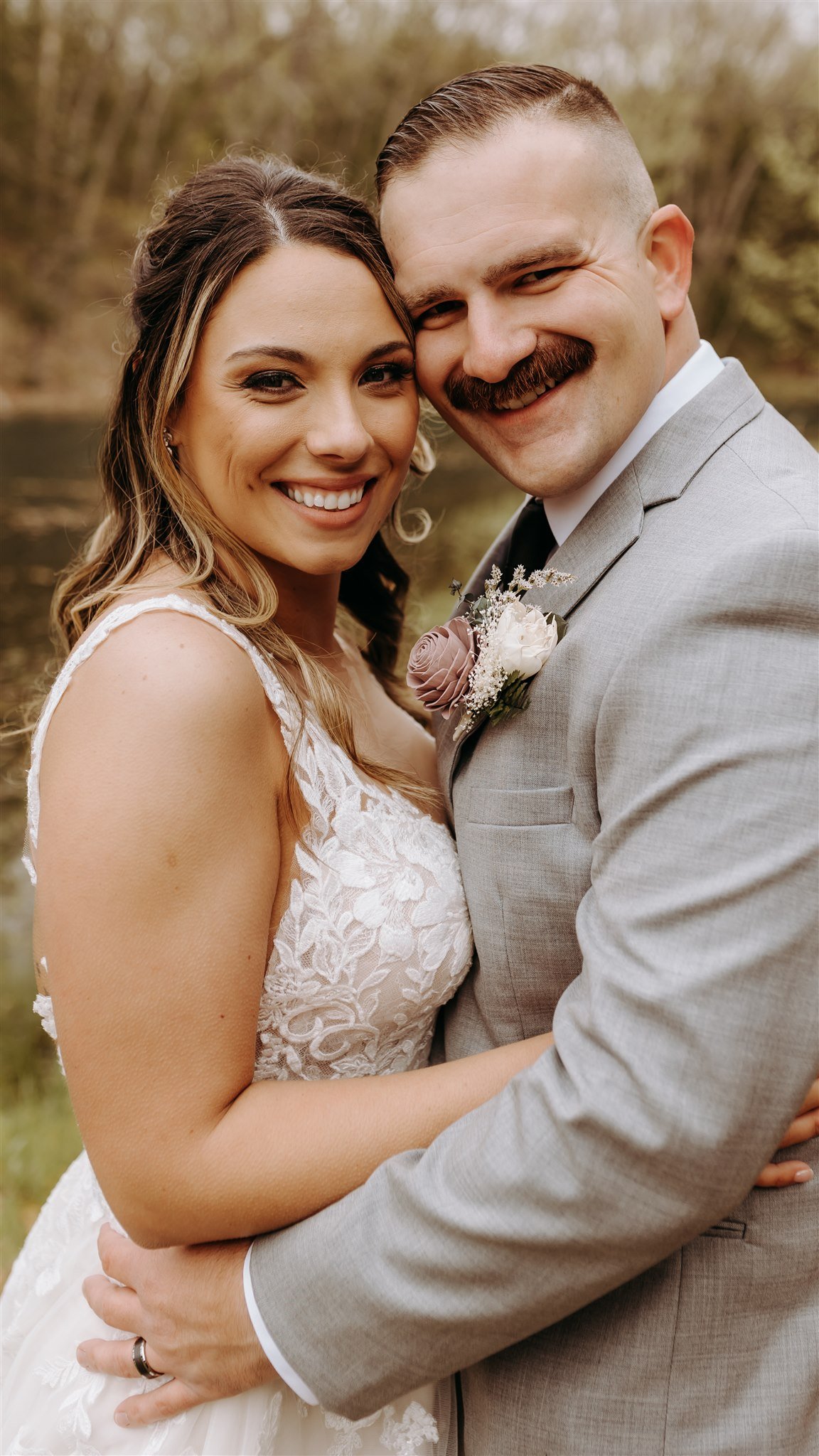 A bride and groom smiling and hugging outdoors during their wedding, with trees and a river in the background at Rolla, MO rustic wedding venue, The Village. Photos by Columbia, MO Photographer Liv Strange Photography.