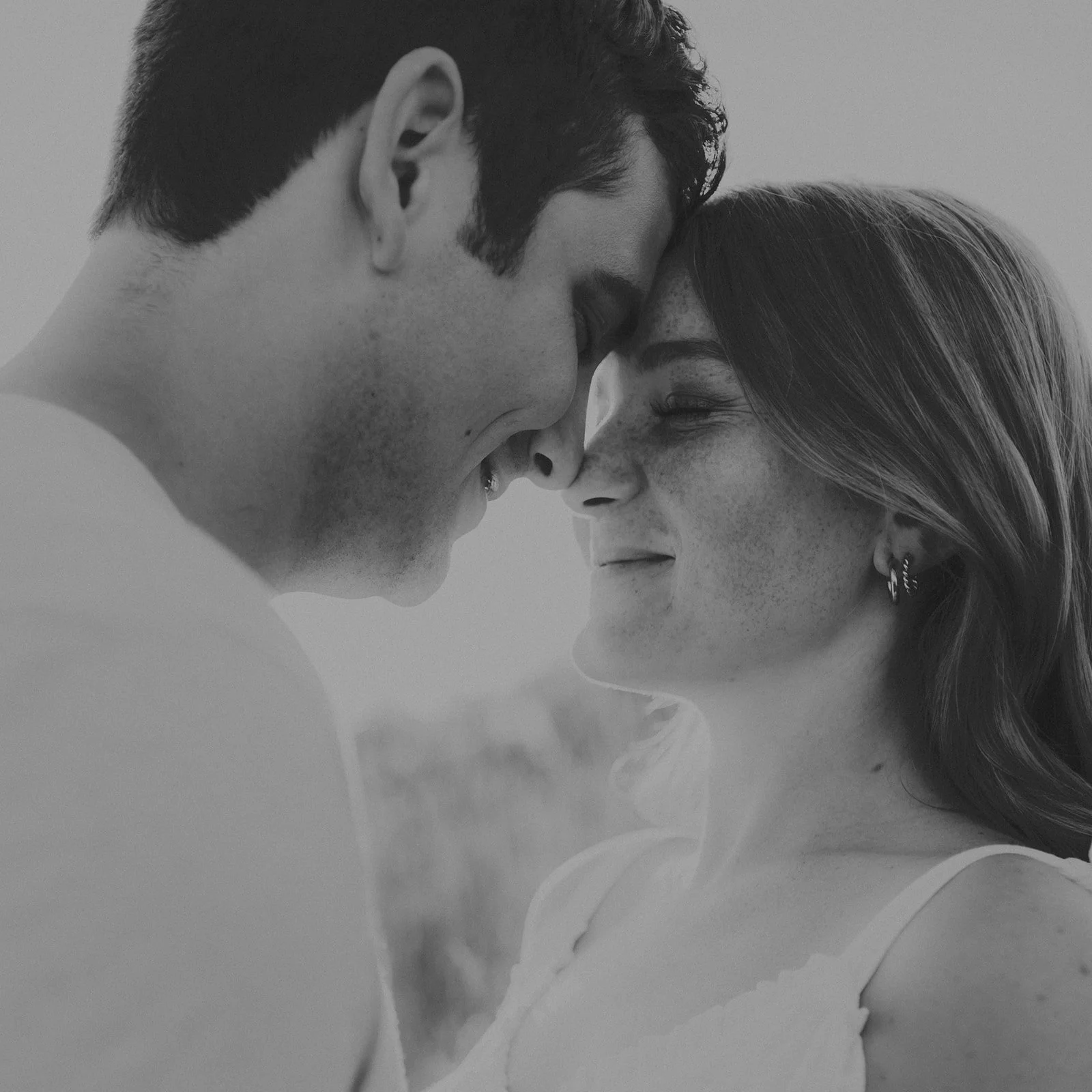 A black and white close-up photo of a couple with their foreheads touching, smiling softly, with the man's face close to the woman's face during their engagement photography session at Rock Bridge State Park in Columbia, MO.