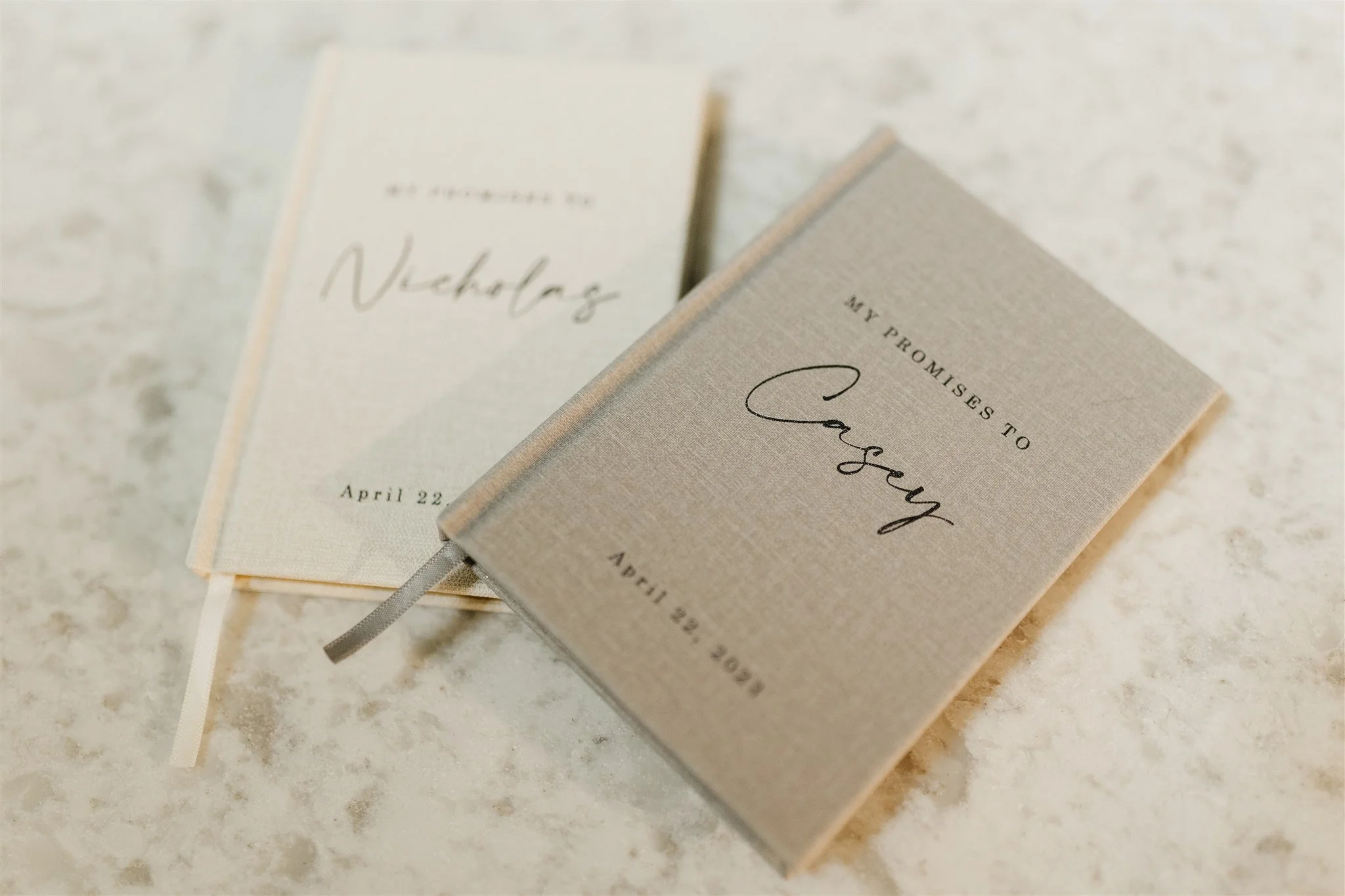 Two beige wedding vows booklets on a light-colored stone surface at Rolla, Missouri rustic wedding venue, The Village. Photos by Columbia, MO Photographer Liv Strange Photography.