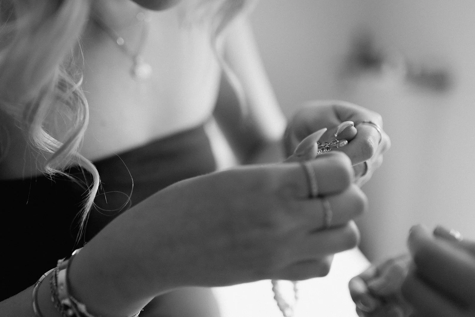 A woman with curly hair is holding a string of beads or jewelry, with her hands and part of her face visible, in black and white at an intimate backyard wedding in Columbia, MO.
