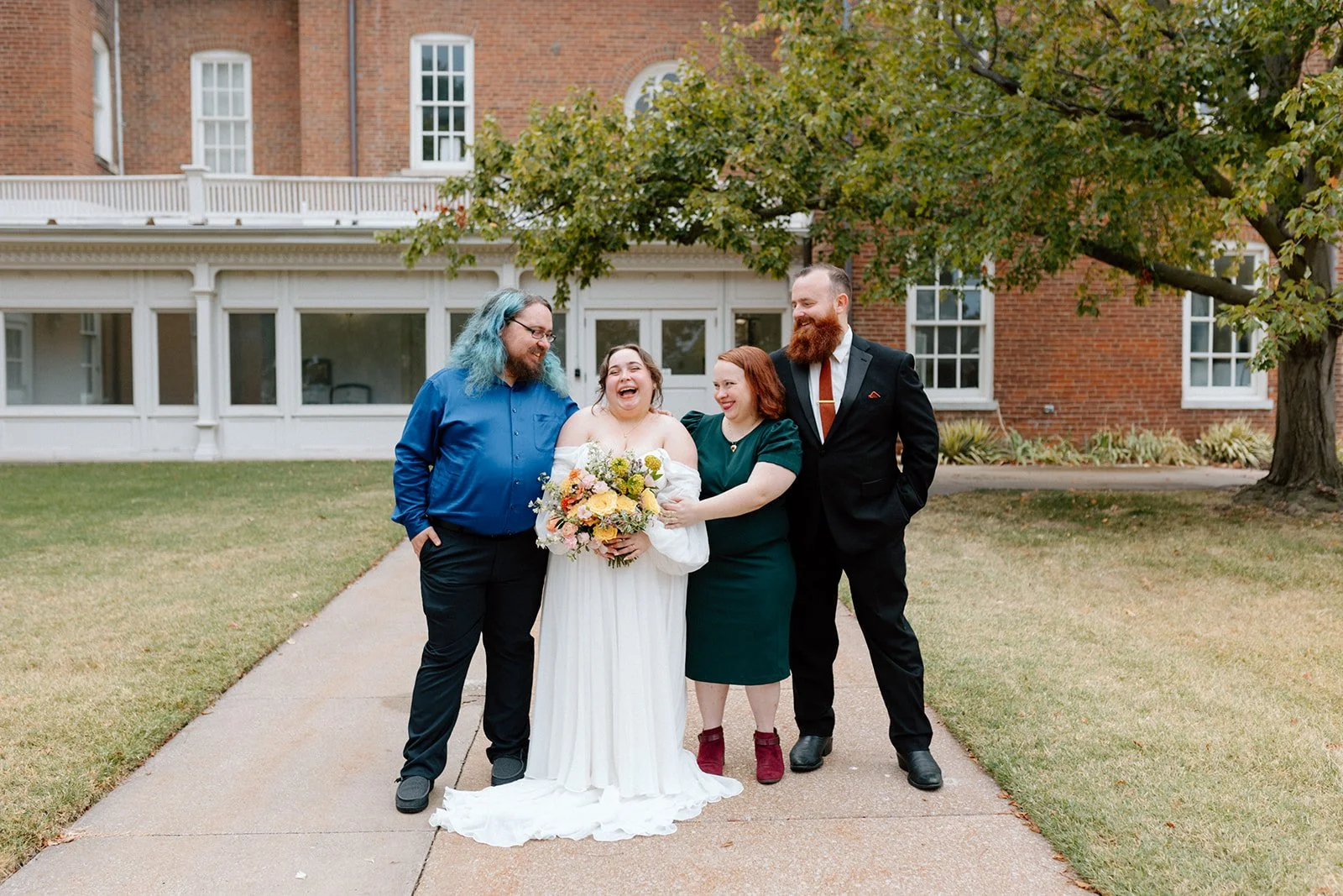 Group of four people smiling together with a bride at an LGBTQ+ wedding in Columbia, MO at wedding venue, Stephens College Senior Hall.
