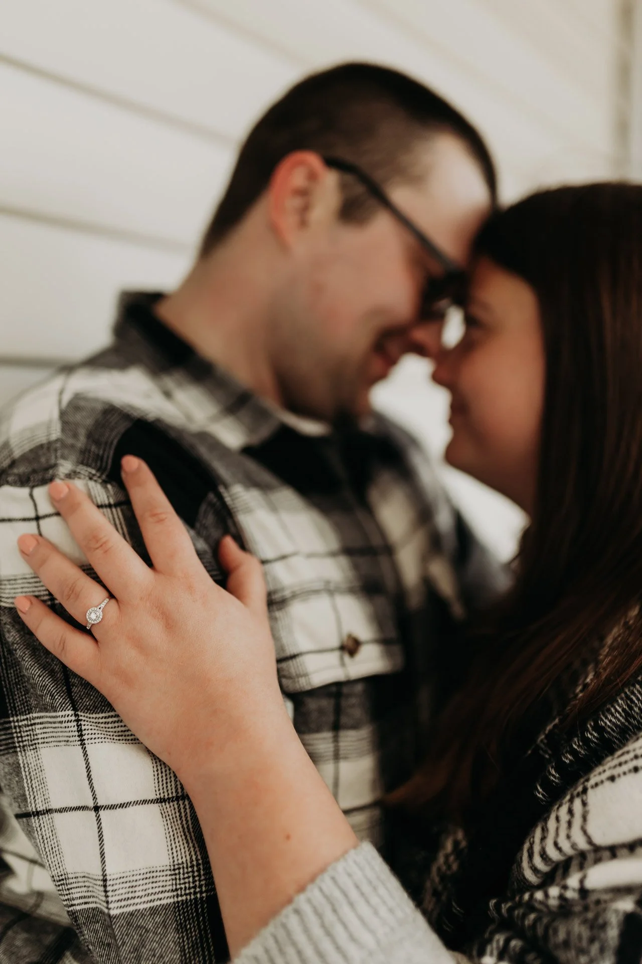 Close-up of a couple touching foreheads, the woman showing an engagement ring on her finger at their engagement photography session at Queeny Park in STL.