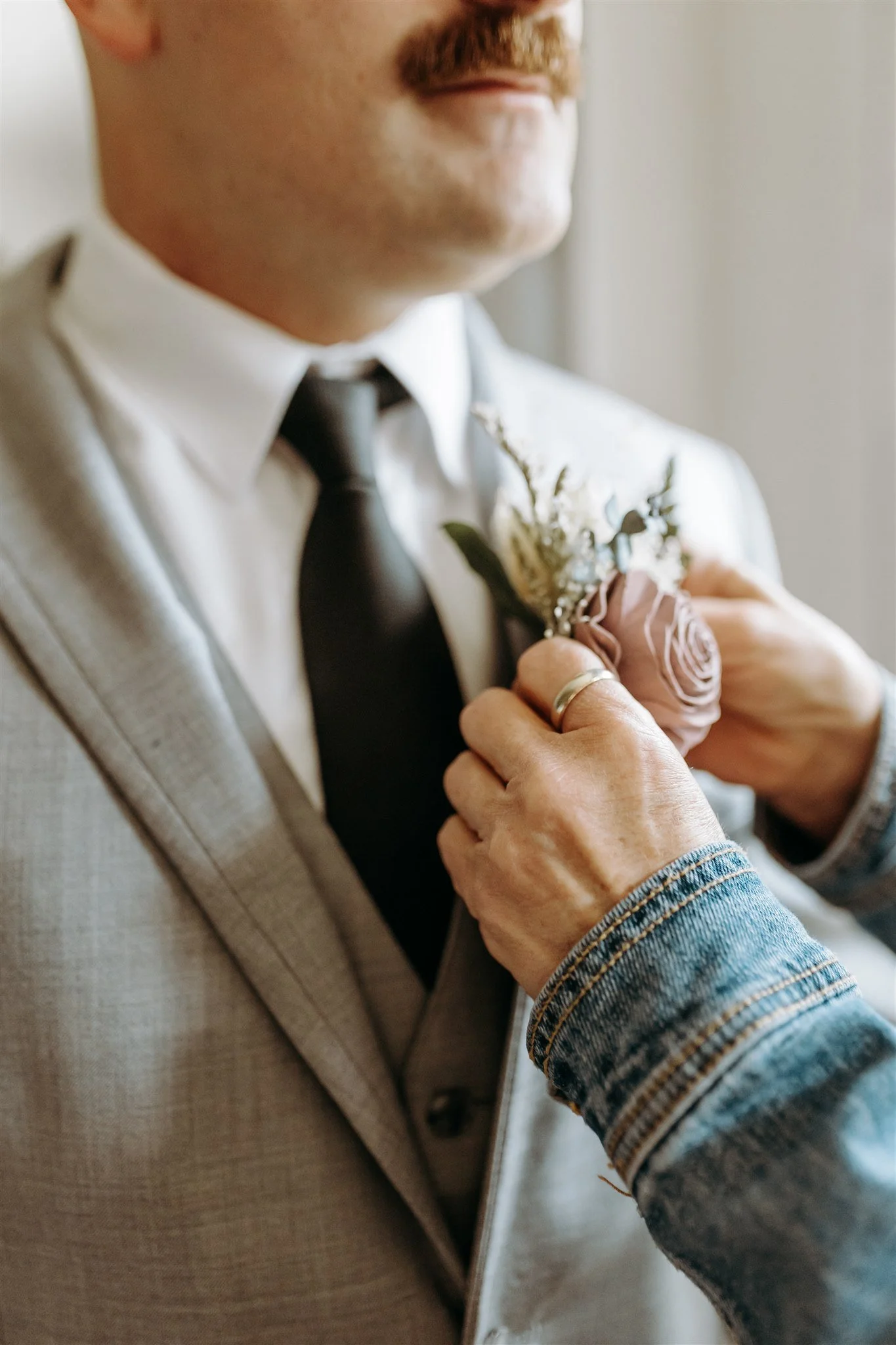 A groom wearing a wedding suit with a boutonniere being pinned by another person at Rolla, Missouri rustic wedding venue, The Village. Photos by Columbia, MO Photographer Liv Strange Photography.
