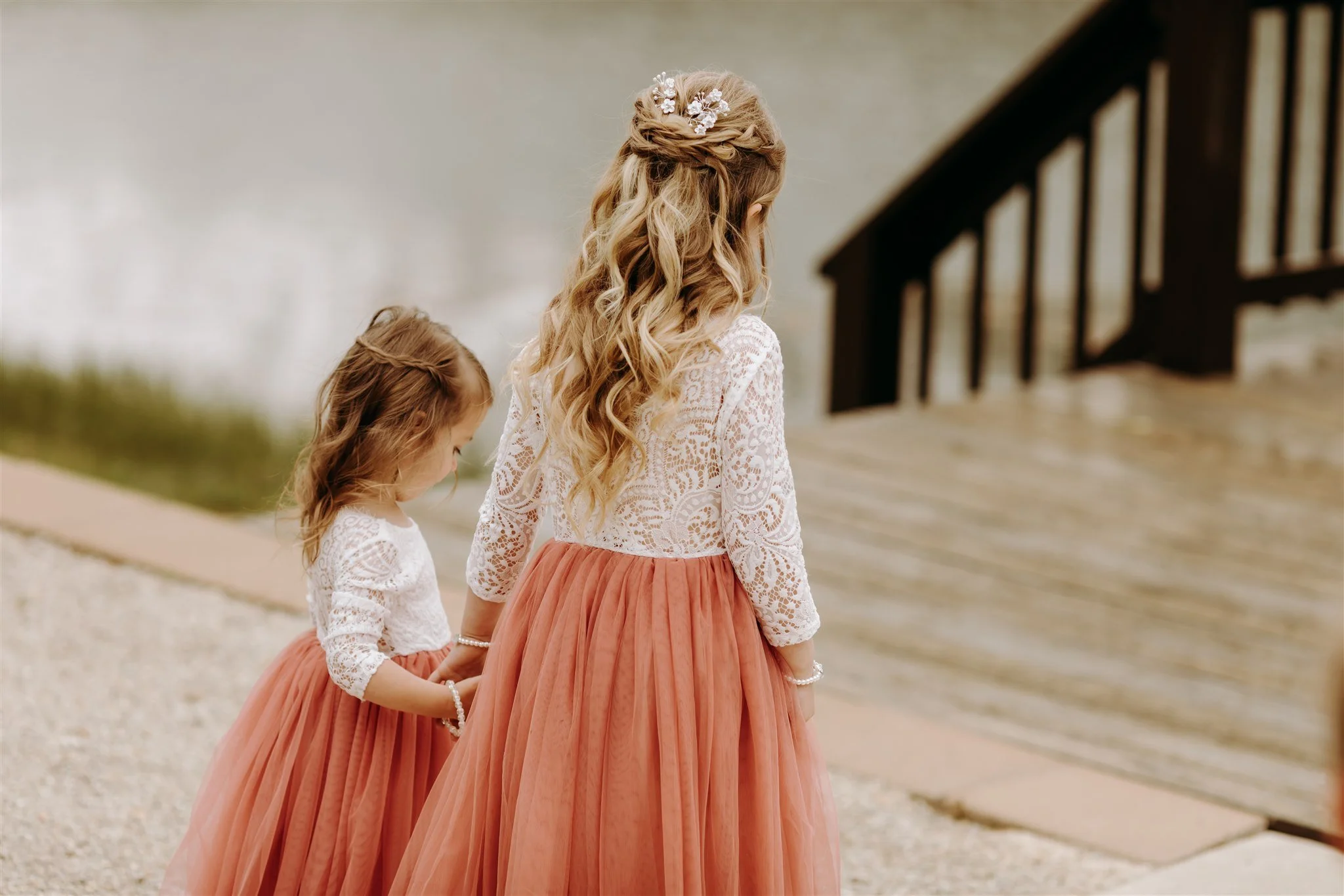 Two young flower girls in matching white lace tops and peach tulle skirts standing during a wedding ceremony at Rolla, Missouri rustic wedding venue, The Village. Photos by Columbia, MO Photographer Liv Strange Photography.