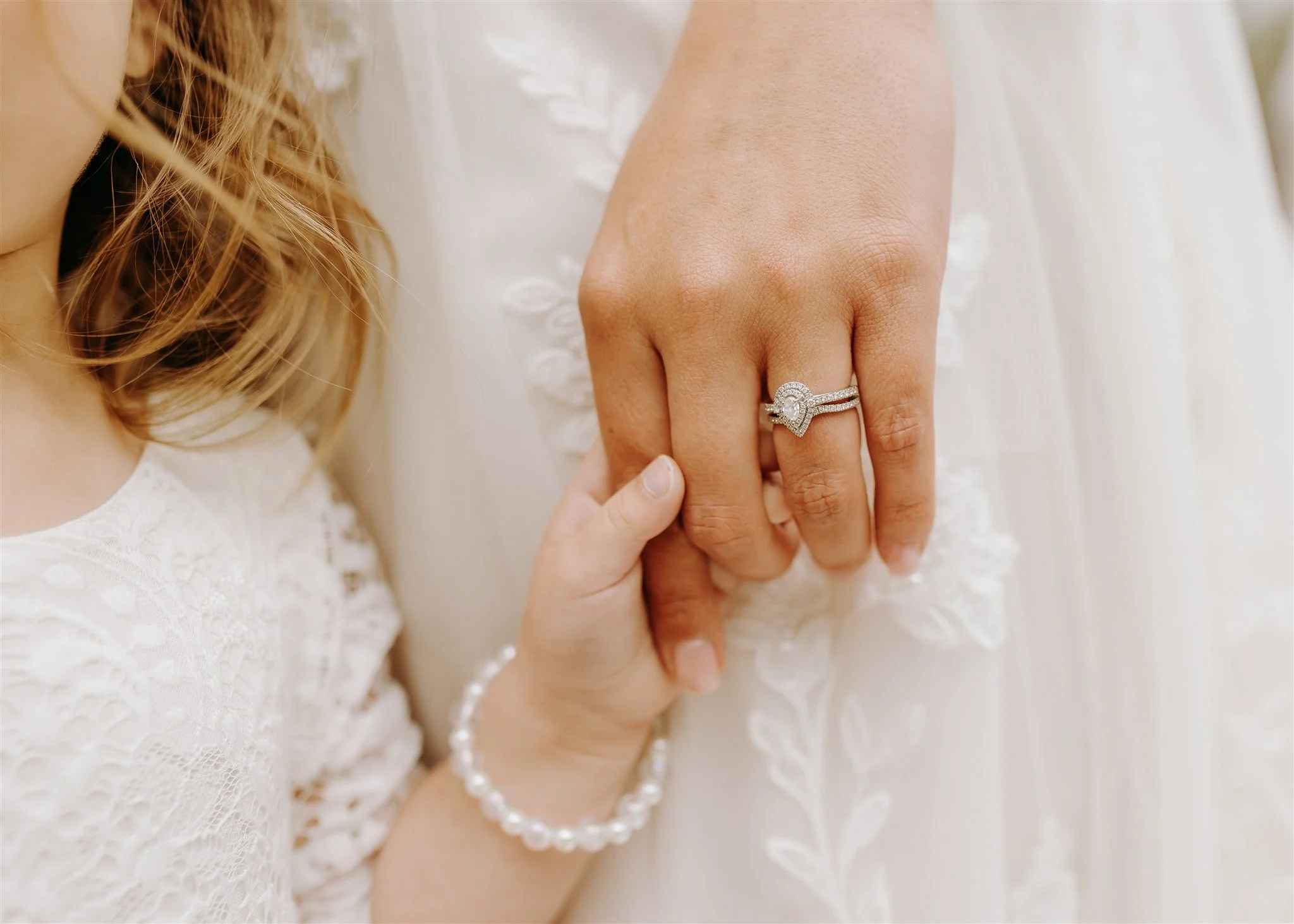 Close-up of a woman's hand with a wedding ring and engagement ring, holding a child's hand with a pearl bracelet at Rolla, Missouri rustic wedding venue, The Village. Photos by Columbia, MO Photographer Liv Strange Photography.