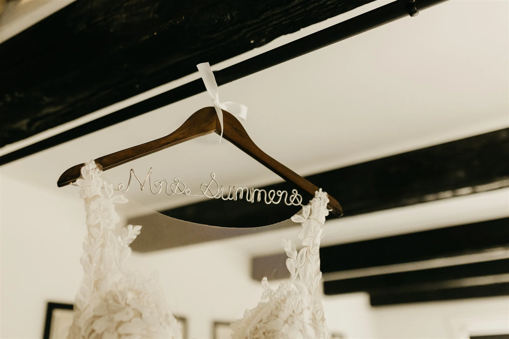 Wedding dress hanging on a wooden hanger with a wire sign that says "Mrs. Summers" at Rolla, Missouri rustic wedding venue, The Village. Photos by Columbia, MO Photographer Liv Strange Photography.
