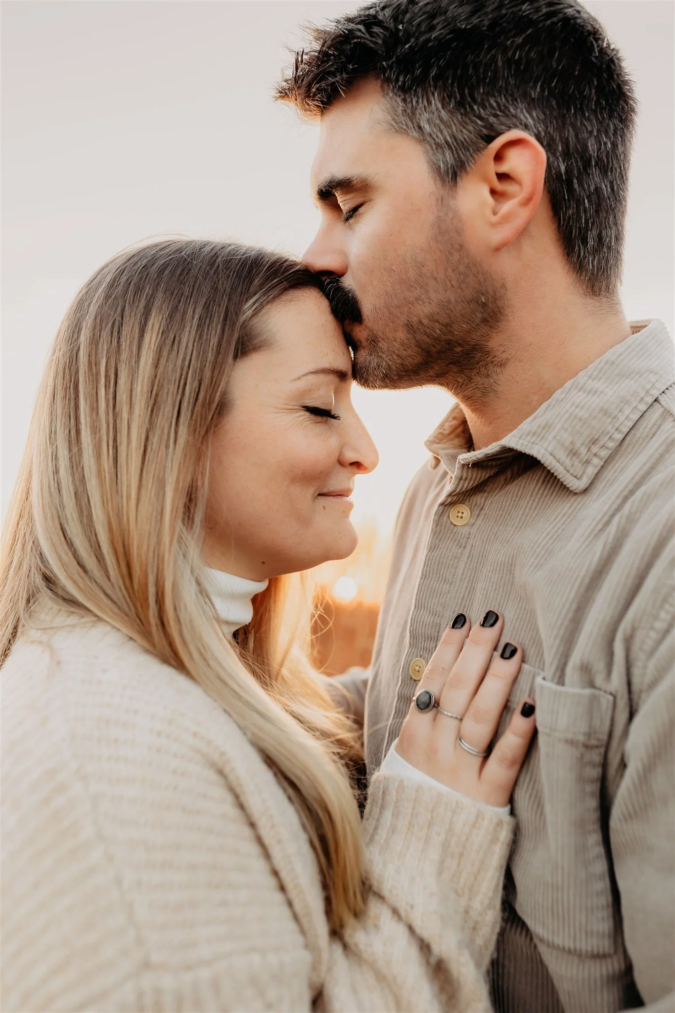 A couple sharing a tender moment outdoors at sunset, with the man kissing the woman's forehead, her eyes closed, both smiling gently during their Columbia, MO couples photography session at Rock Bridge Memorial State Park.