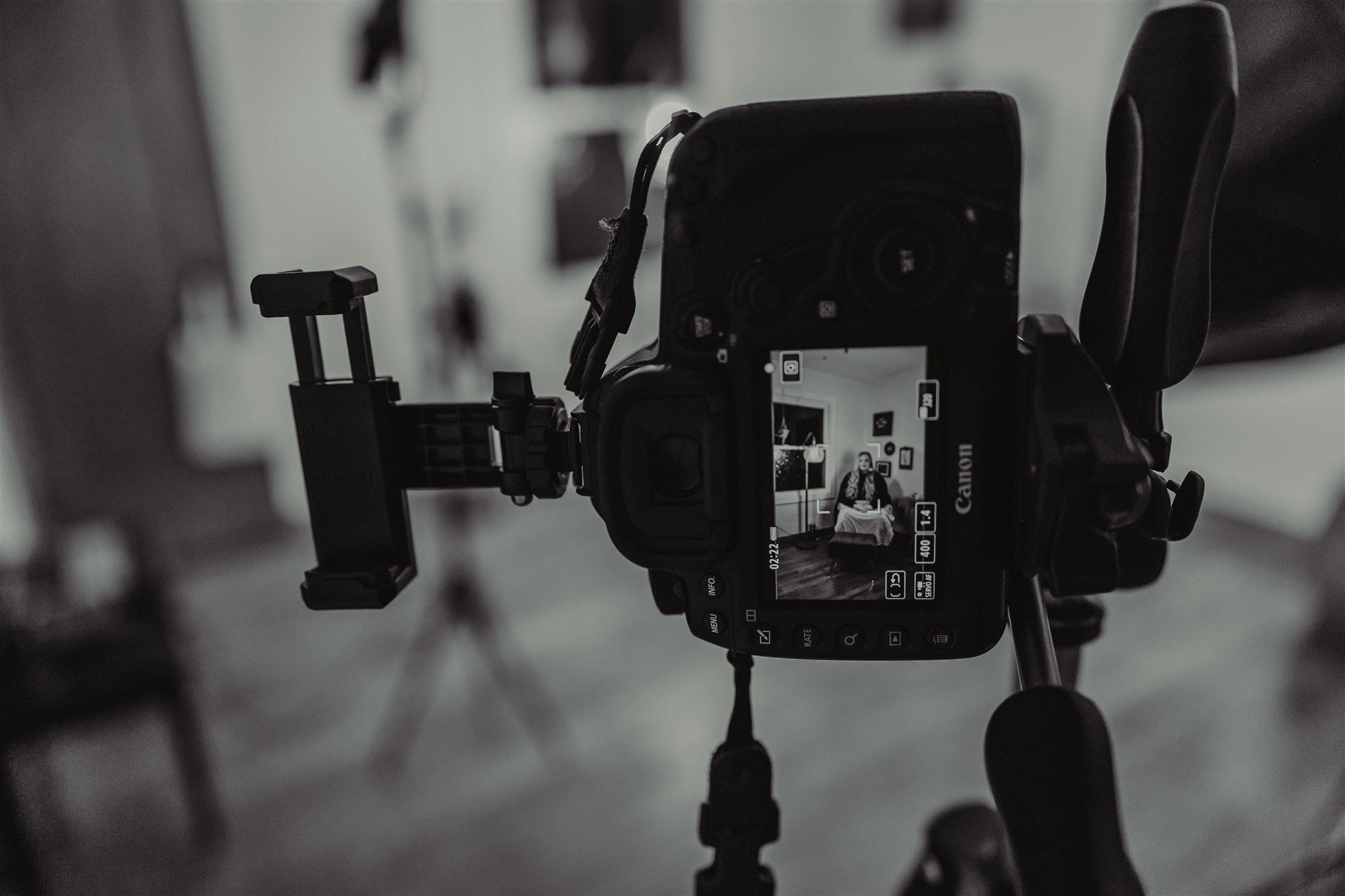 A digital camera on a tripod takes a photo of a woman sitting on a sofa in a room with wall art during a trauma informed photography session in Columbia, Missouri.
