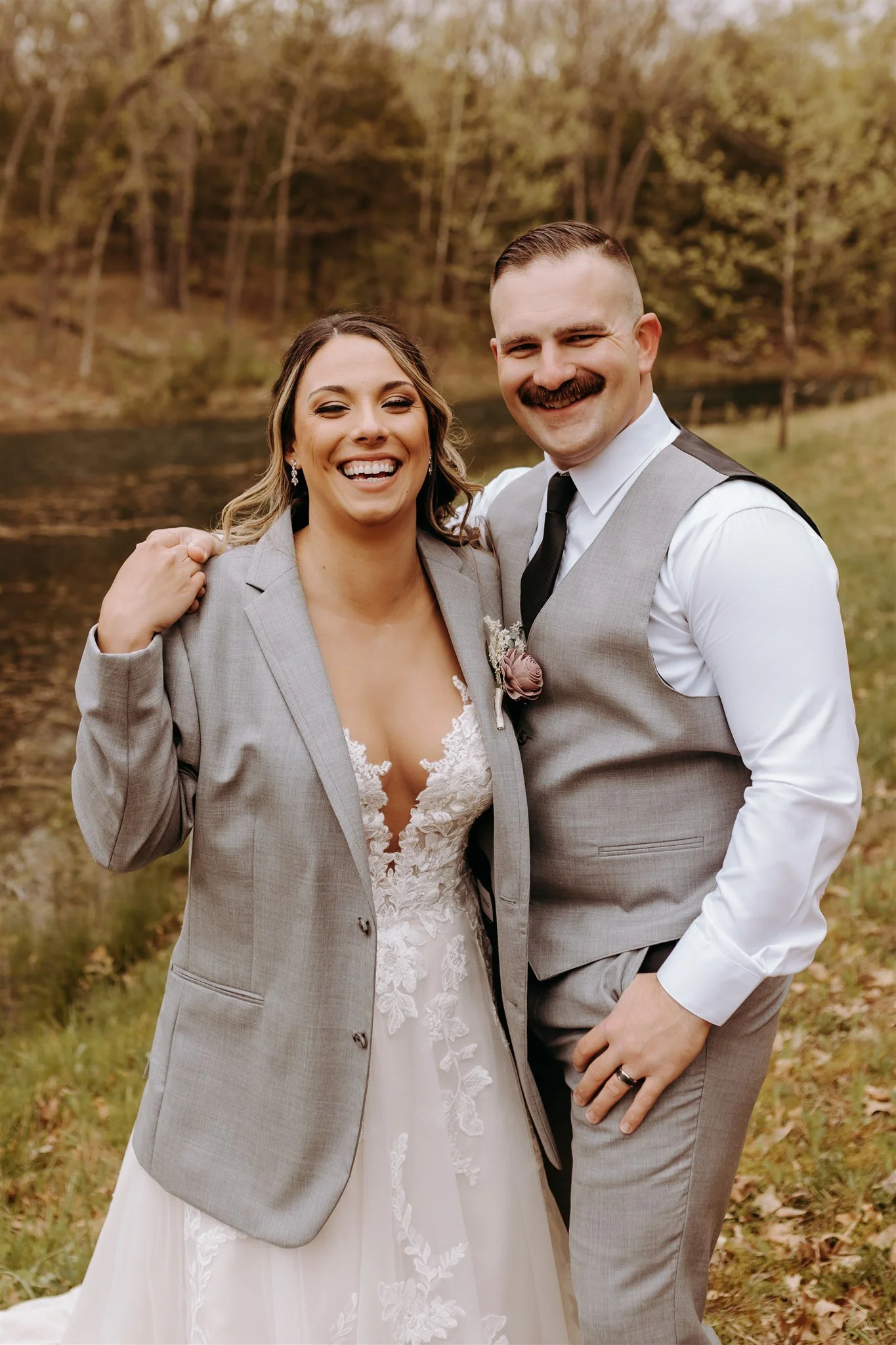 A bride and groom smiling outside by a lake, with trees in the background at Rolla, MO rustic wedding venue, The Village. Photos by Columbia, MO Photographer Liv Strange Photography.