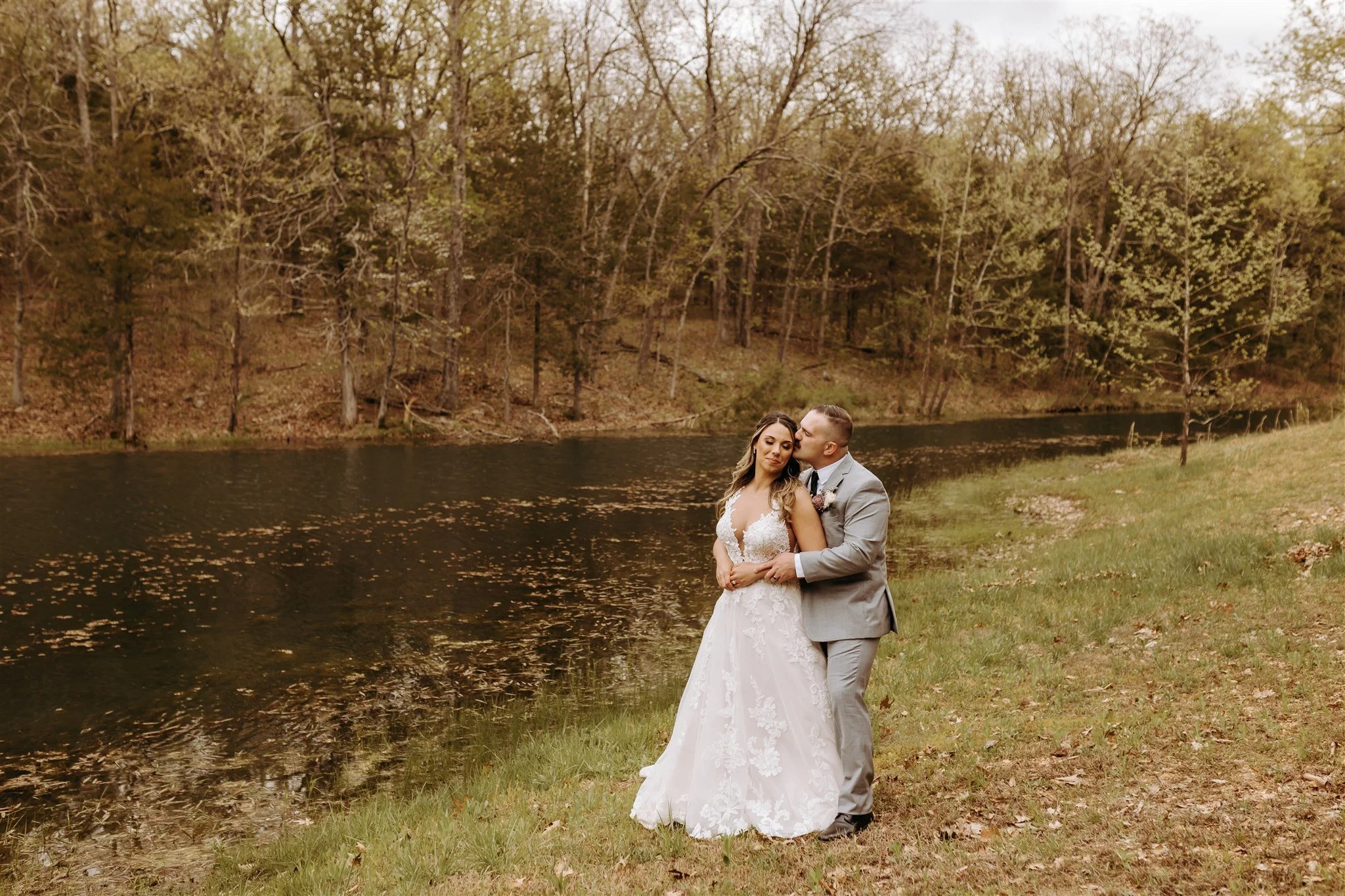 A bride and groom standing near a river with trees in the background, during sunset at Rolla, MO rustic wedding venue, The Village. Photos by Columbia, MO Photographer Liv Strange Photography.