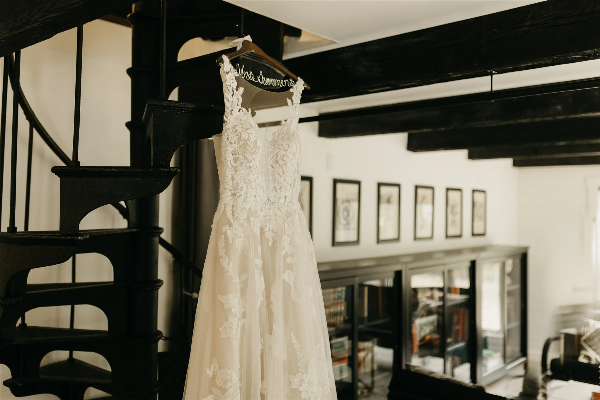 A wedding dress hanging on a hanger on a staircase railing in a living room at Rolla, MO rustic wedding venue, The Village.