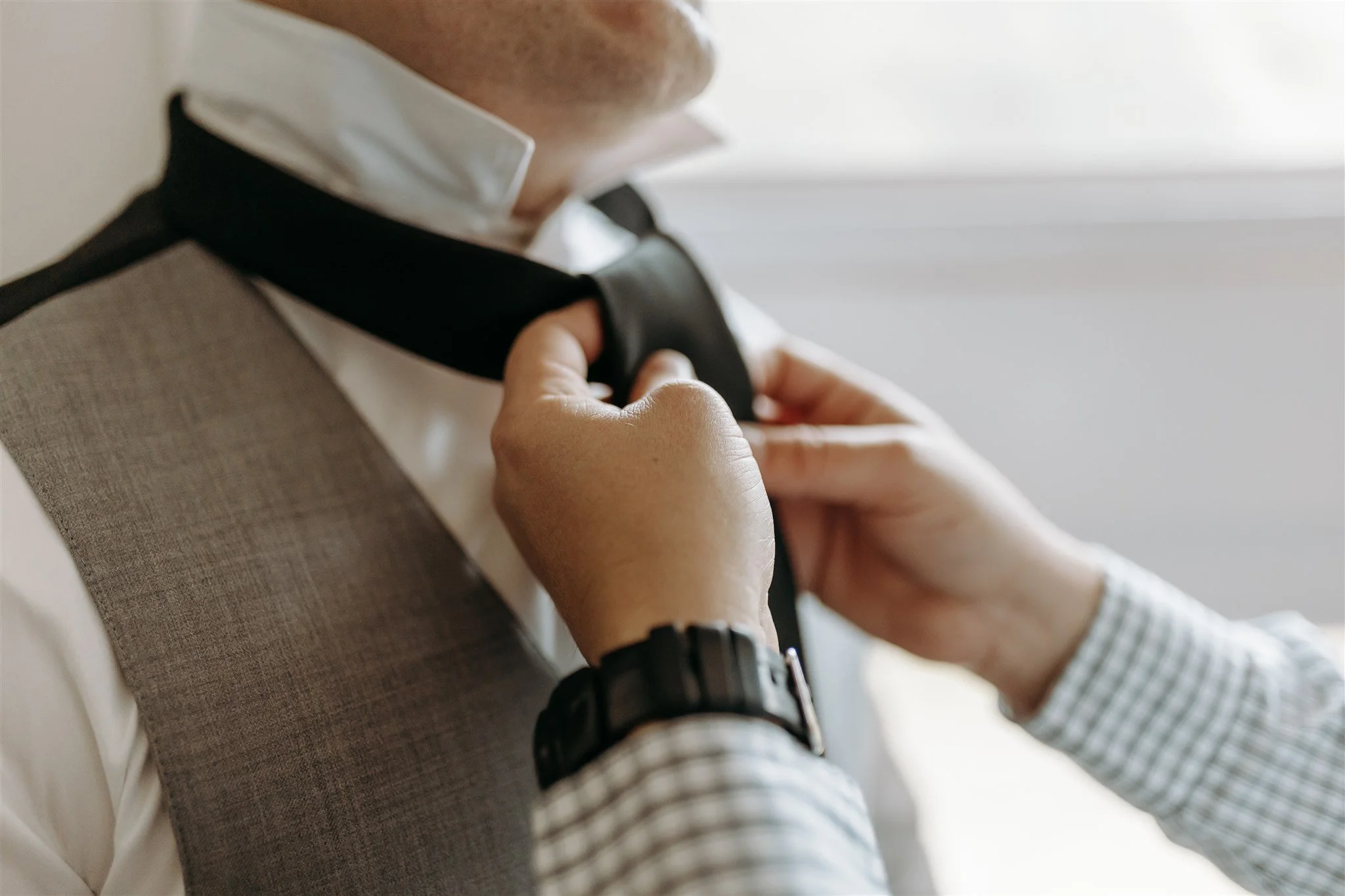 A person adjusting a black bow tie around their neck, dressed in a white shirt and a gray vest, with a close-up view of their hands at Rolla, Missouri rustic wedding venue, The Village. Photos by Columbia, MO Photographer Liv Strange Photography.
