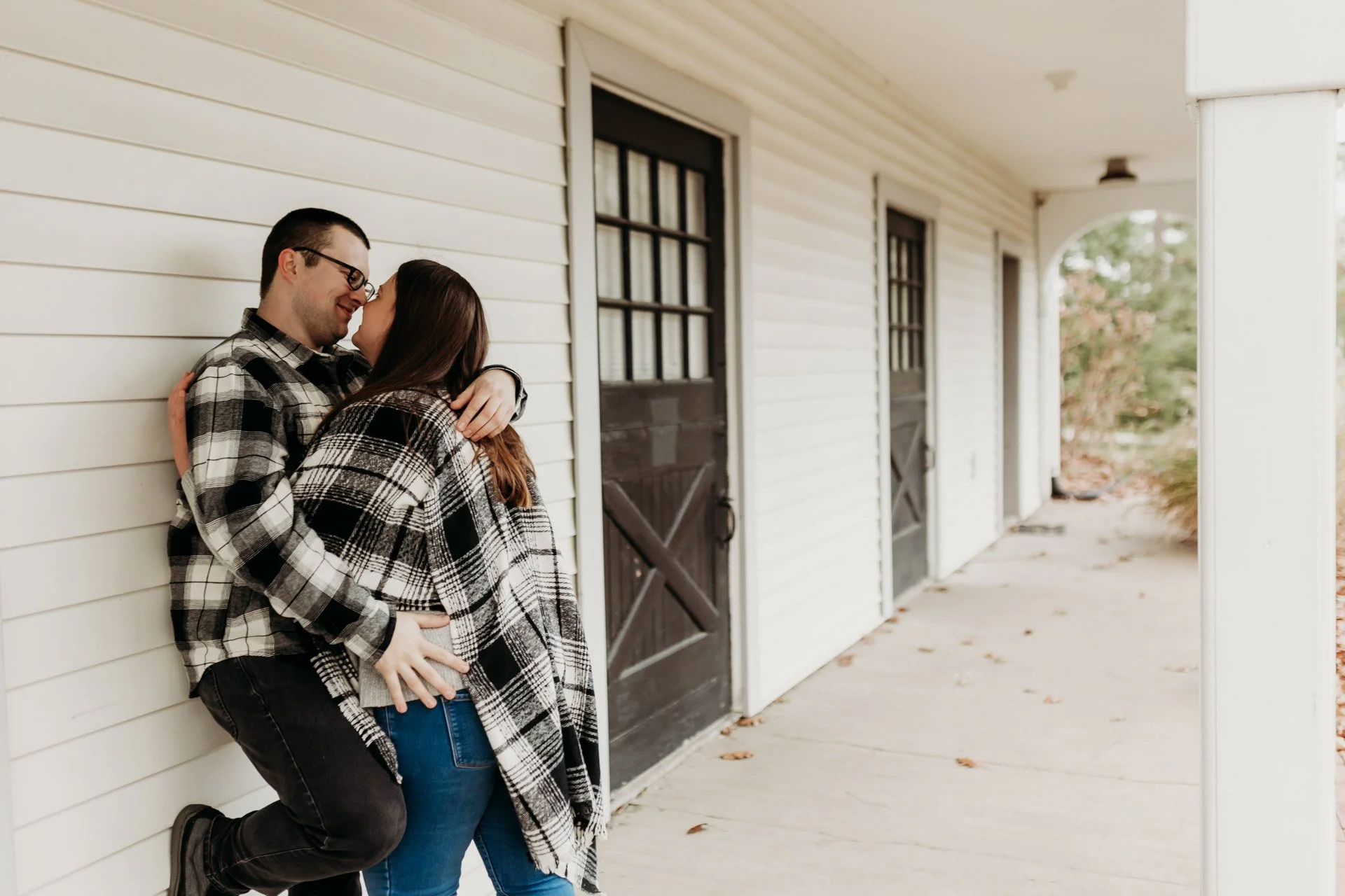 A couple sharing an intimate moment on a porch, embracing and touching noses, with their eyes closed at their engagement photography session at Queeny Park in STL.